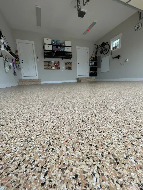 Spacious garage interior with speckled concrete floor, storage shelves, doors, and wall-mounted equipment