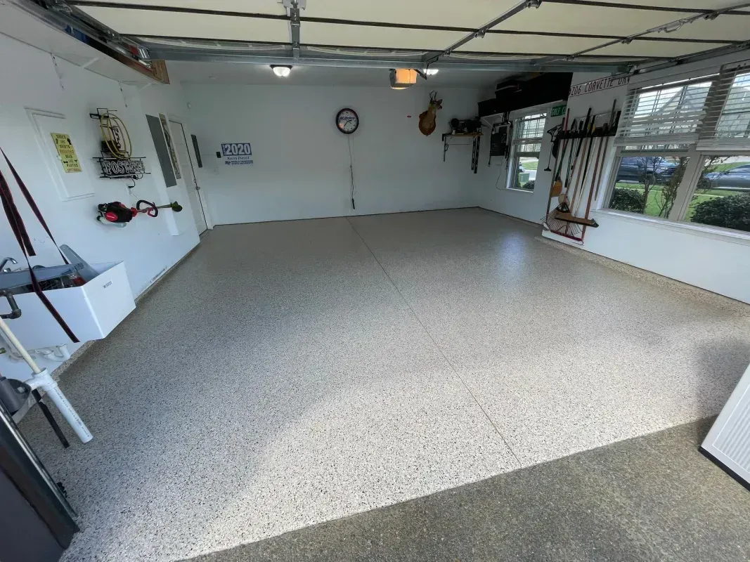 Empty garage with speckled floor, white walls, and windows on the right side.