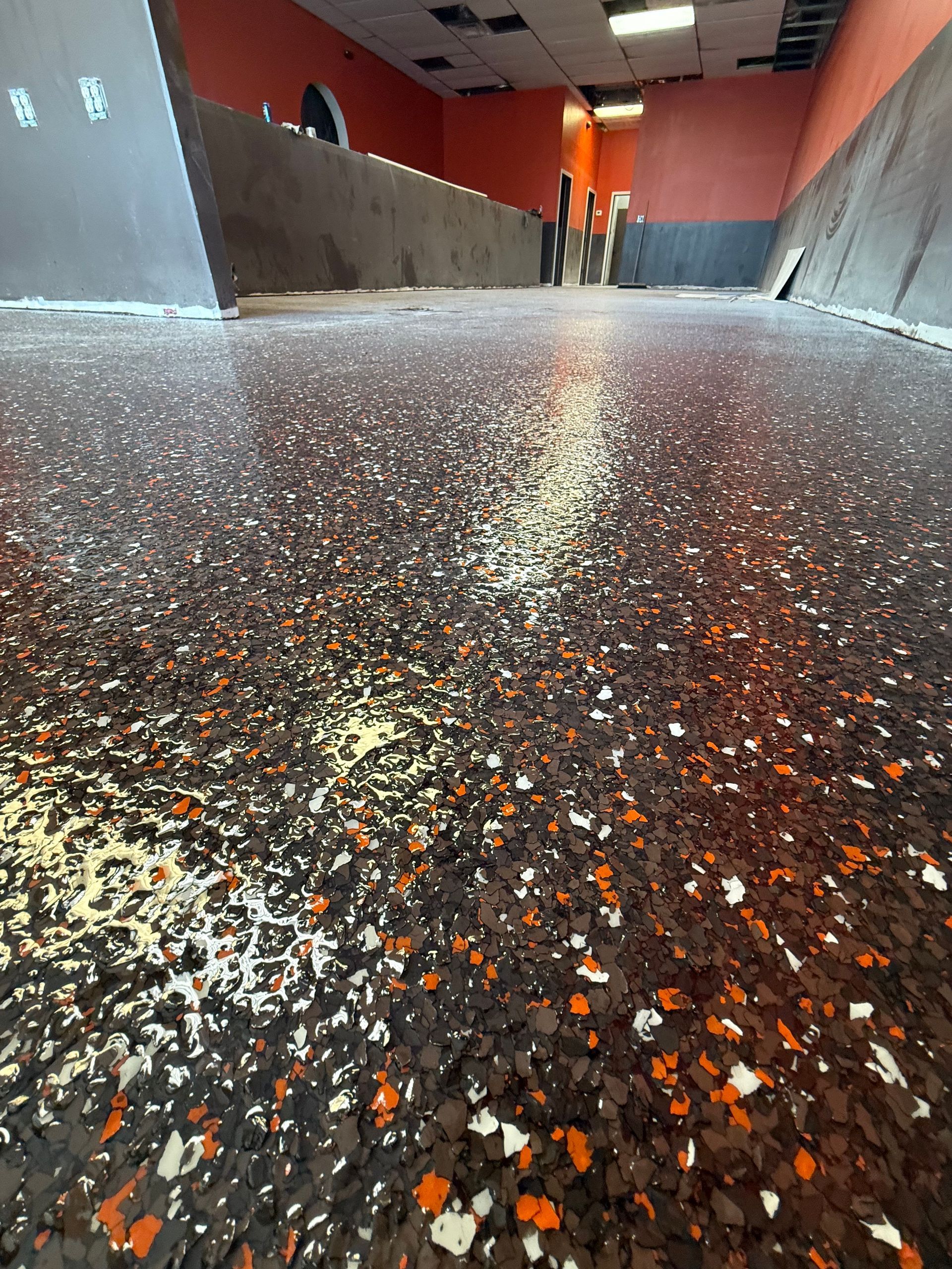 Low-angle view of a speckled terrazzo floor in a hallway with red walls and distant people.