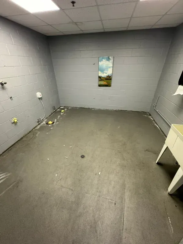 Empty gray room with tiled walls, scattered debris on the floor, and a small wall picture.
