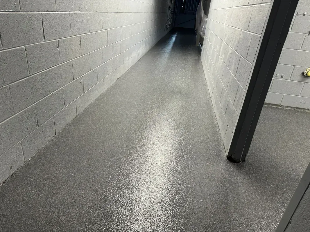 Narrow concrete hallway with white brick walls and a dark doorway at the far end.