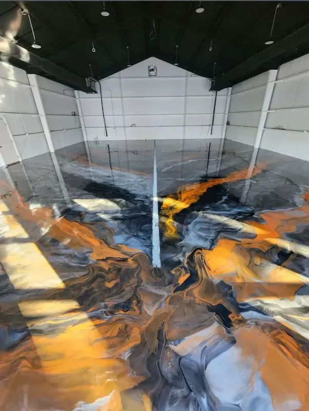 Abstract orange, black, and gray liquid-like swirls in a large indoor tank or pool under a dark roof.