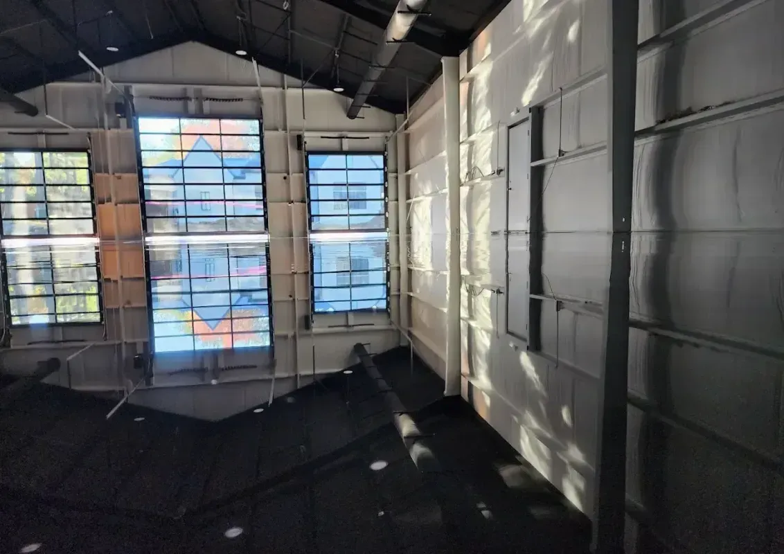 Empty industrial room with metal walls and windows, light streaming onto a dark floor.