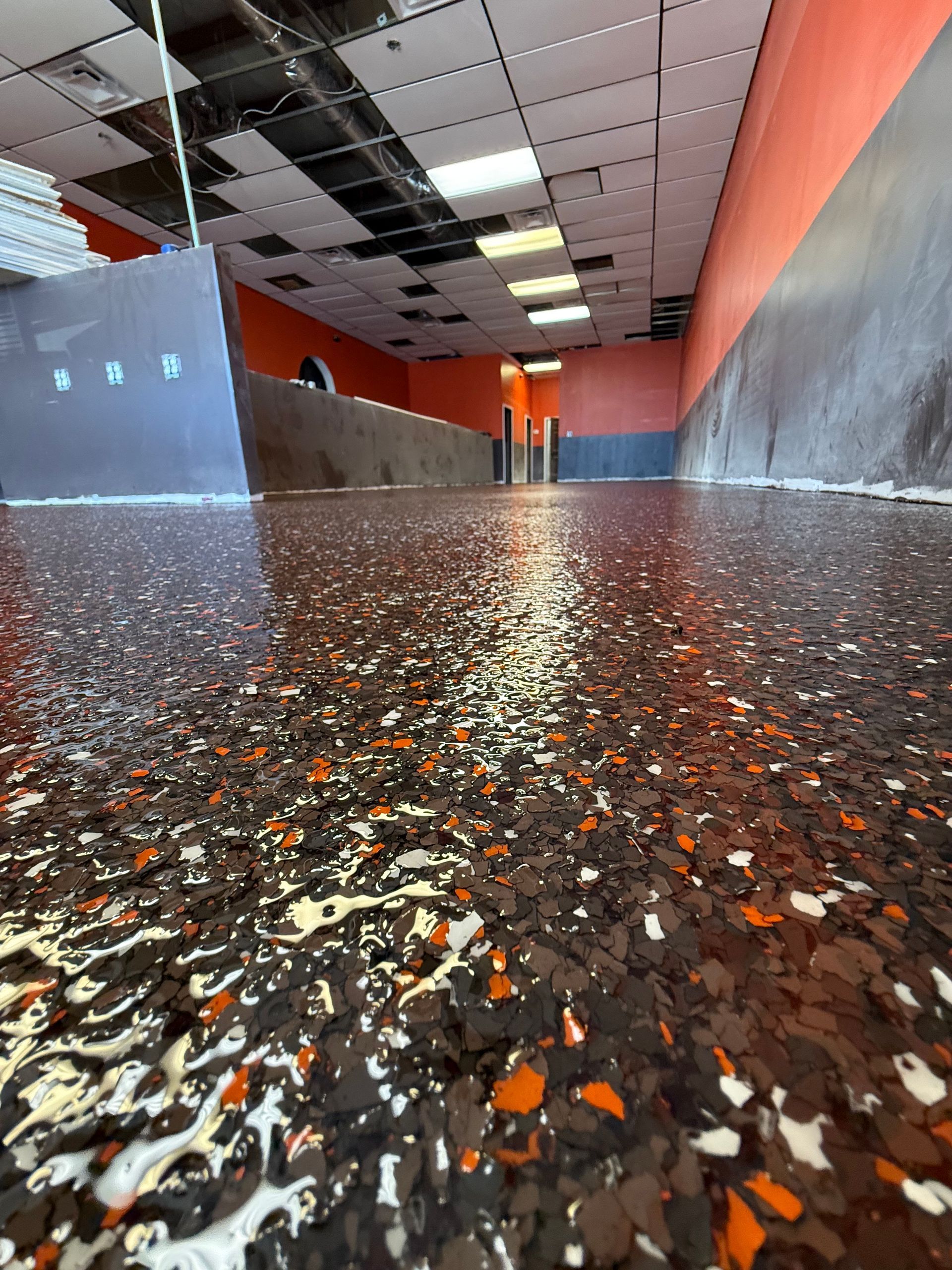 Low-angle view of a wet speckled floor in a hallway with dark walls and a damaged ceiling panel.