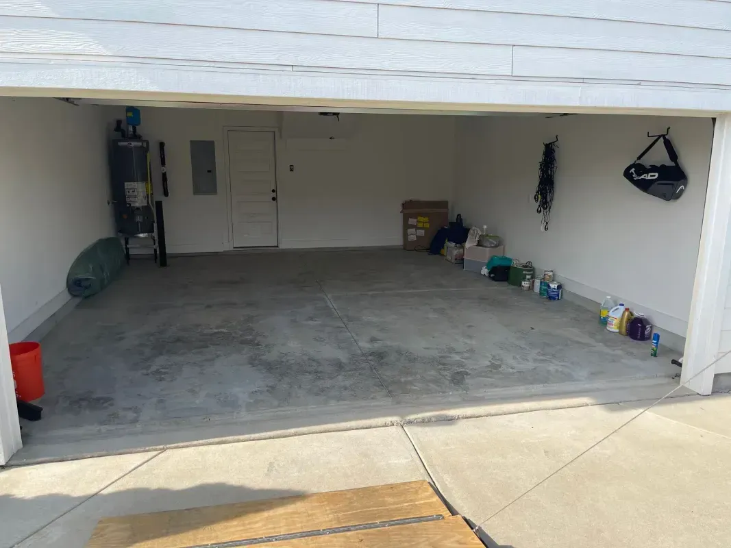 Open garage with empty concrete floor, closed door, and tools stored along the walls.