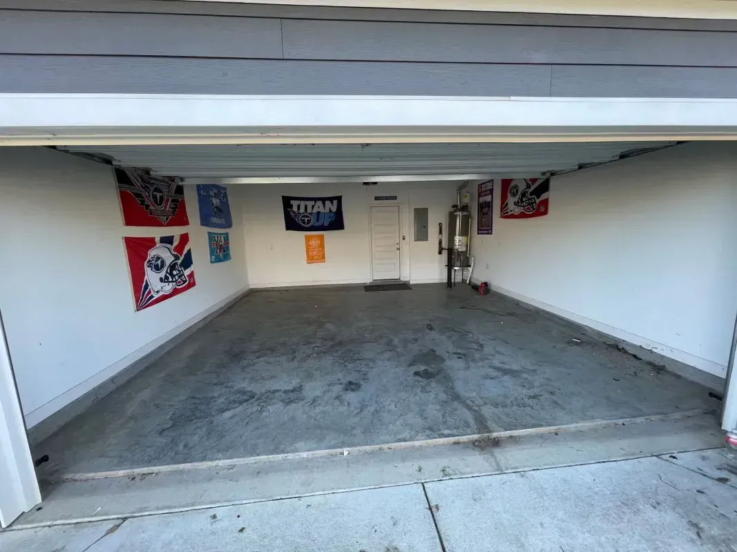 Empty two-car garage with gray concrete floor and white walls, viewed from the open driveway.