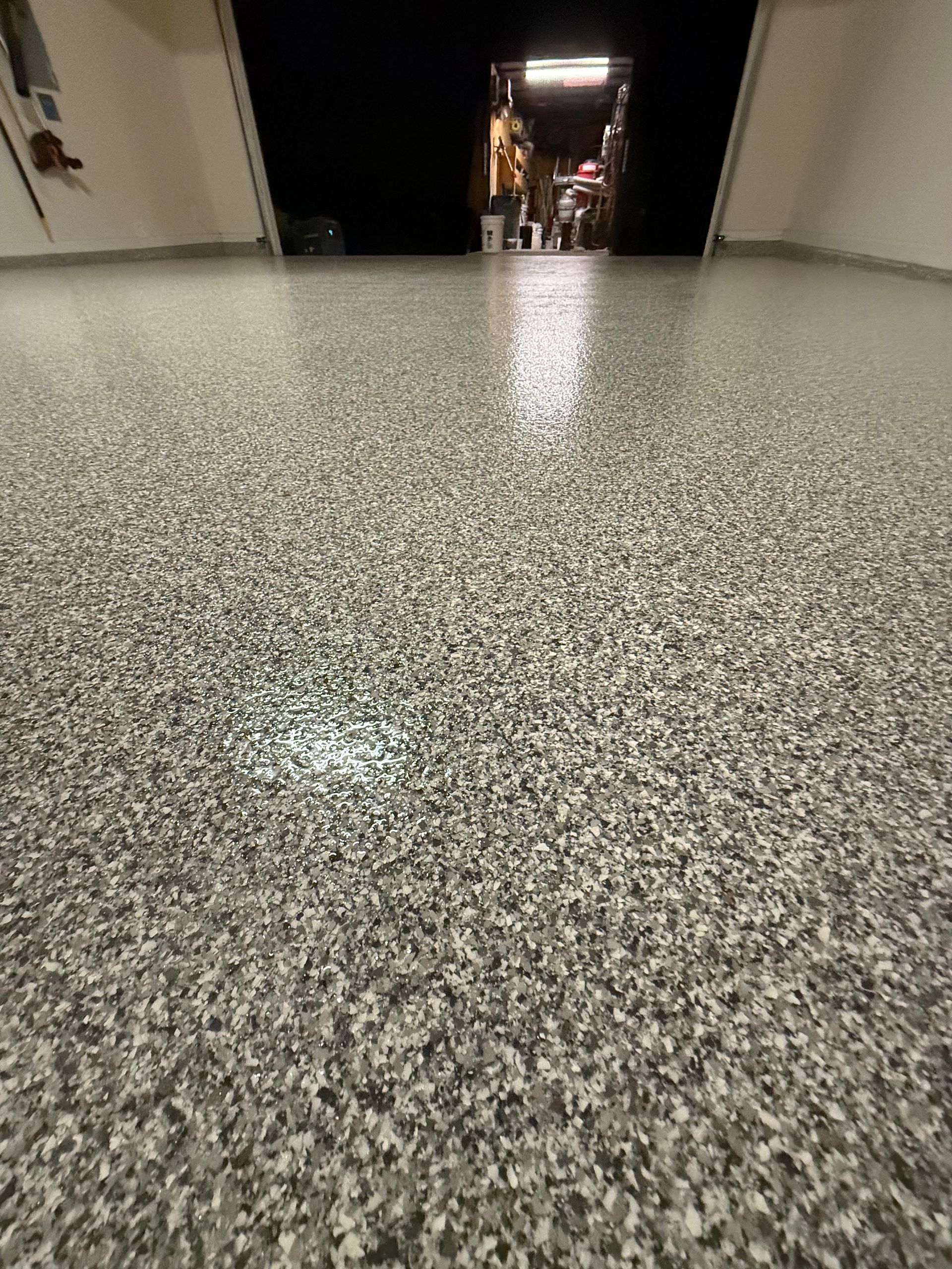 Polished speckled floor in a hallway, leading toward a dark doorway with a small lit area beyond