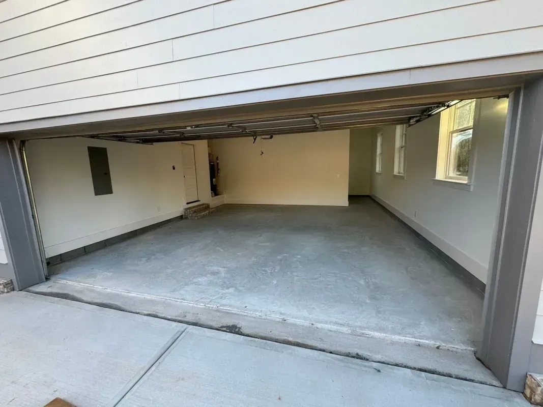 Empty residential garage with open door, concrete floor, and windows along the right wall