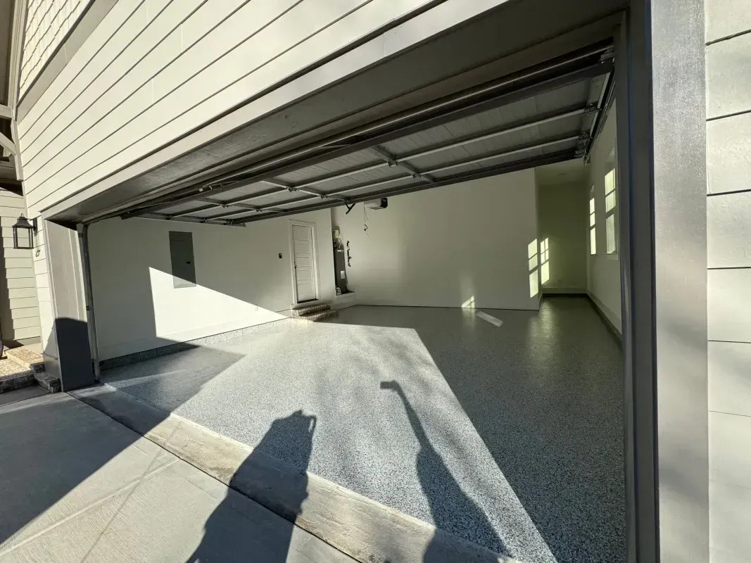 Open garage with empty concrete floor, white walls, and sunlight casting shadows inside