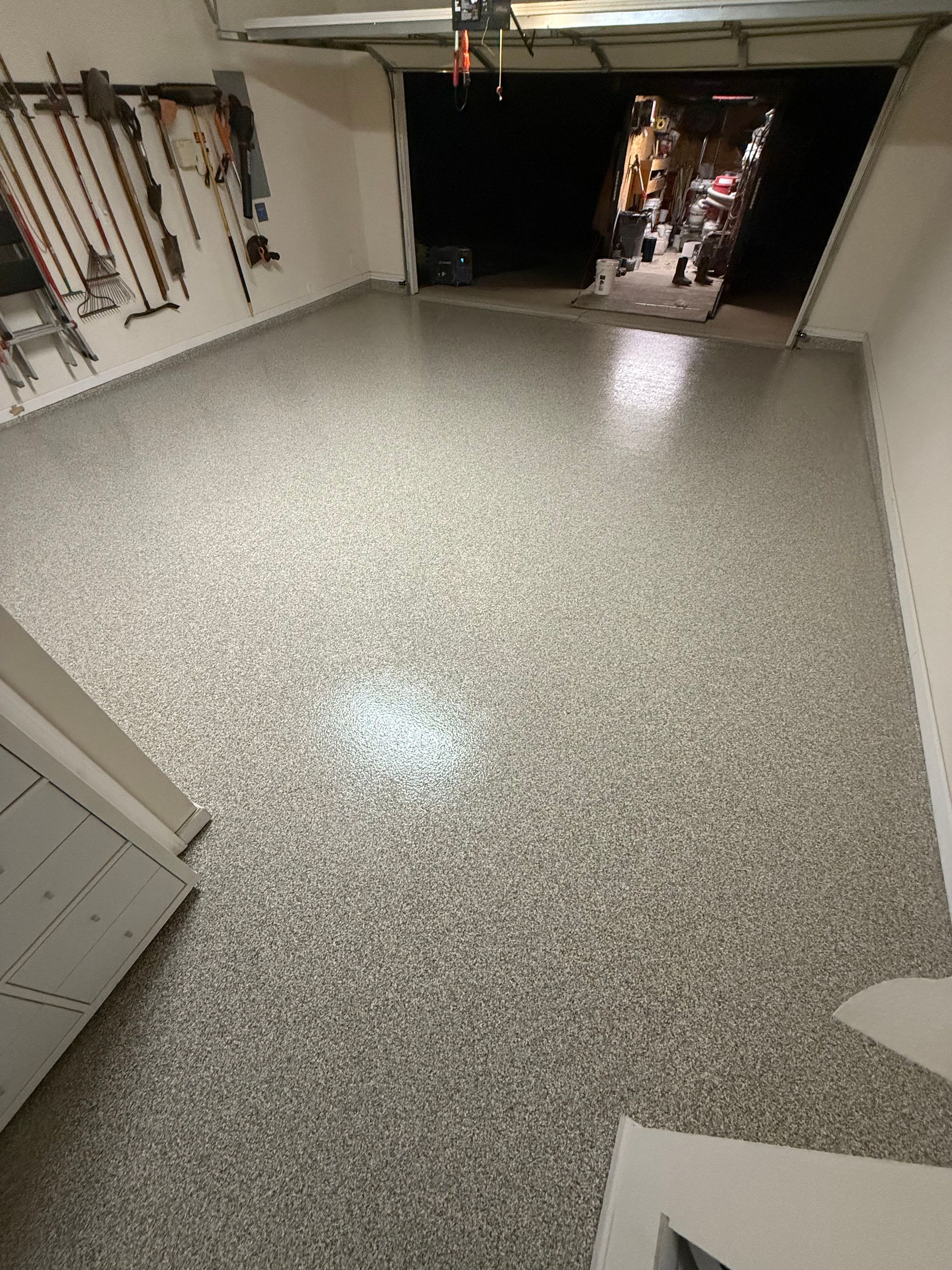 Empty garage with speckled epoxy floor and open doorway to a dim outdoor area