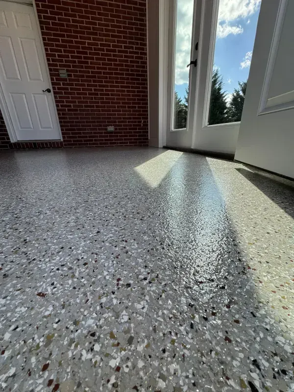Sunlit speckled terrazzo floor by a brick wall and open doors in a room