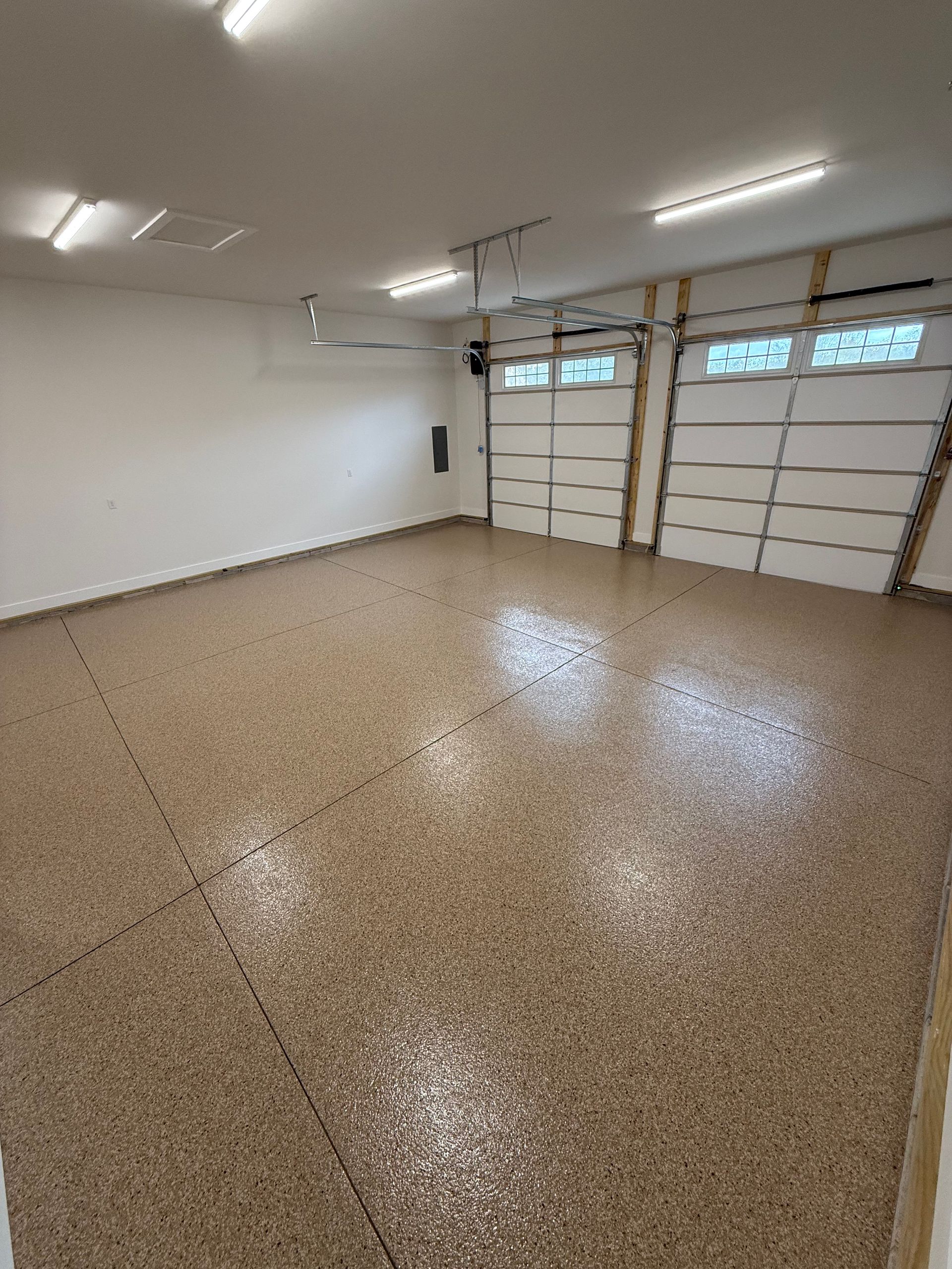Empty garage with white walls, speckled floor, and closed double garage doors.