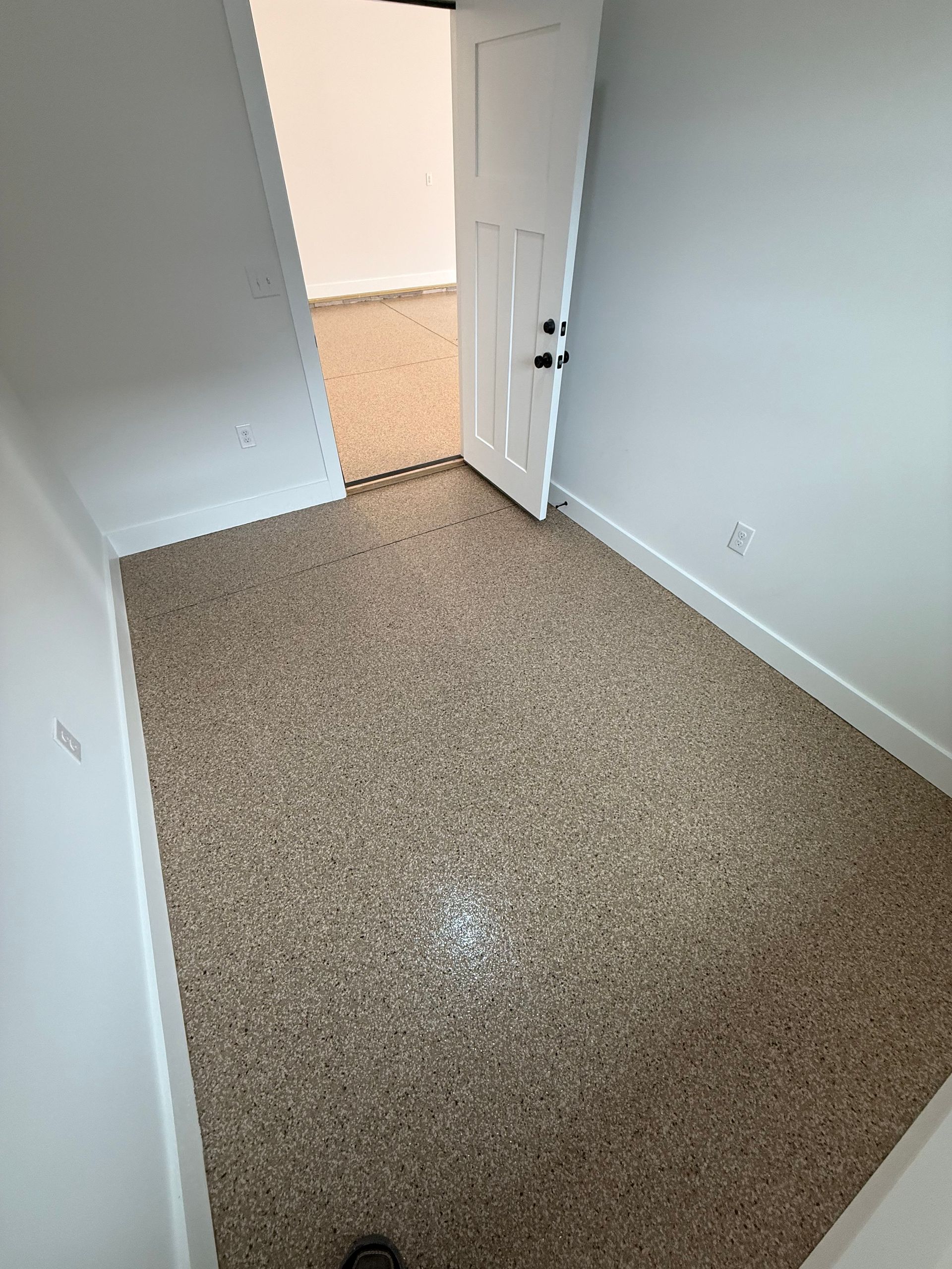 Empty beige-carpeted room with white walls and an open door to a brighter hallway