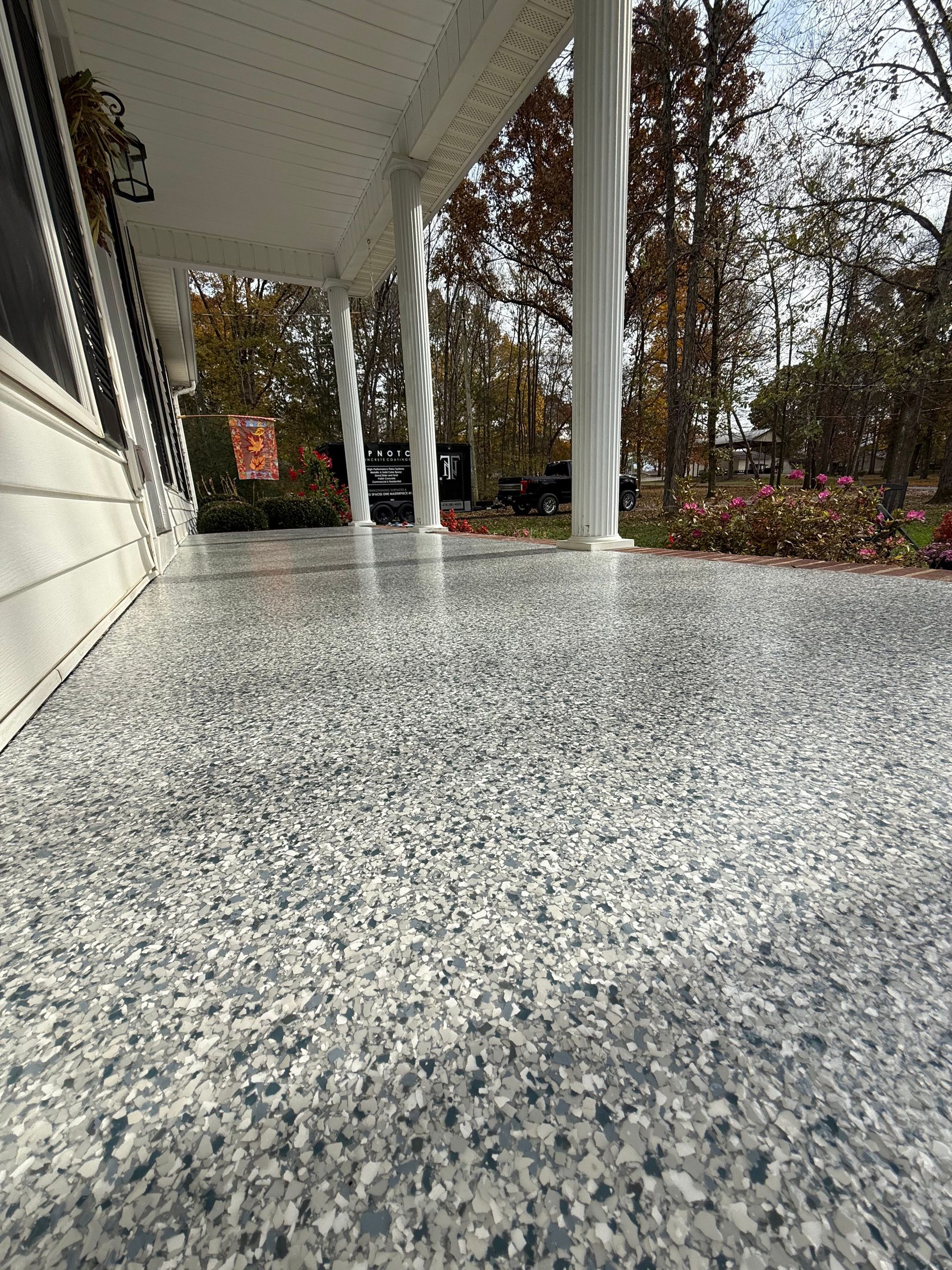Front porch with speckled gray floor, white columns, and autumn trees in the yard.
