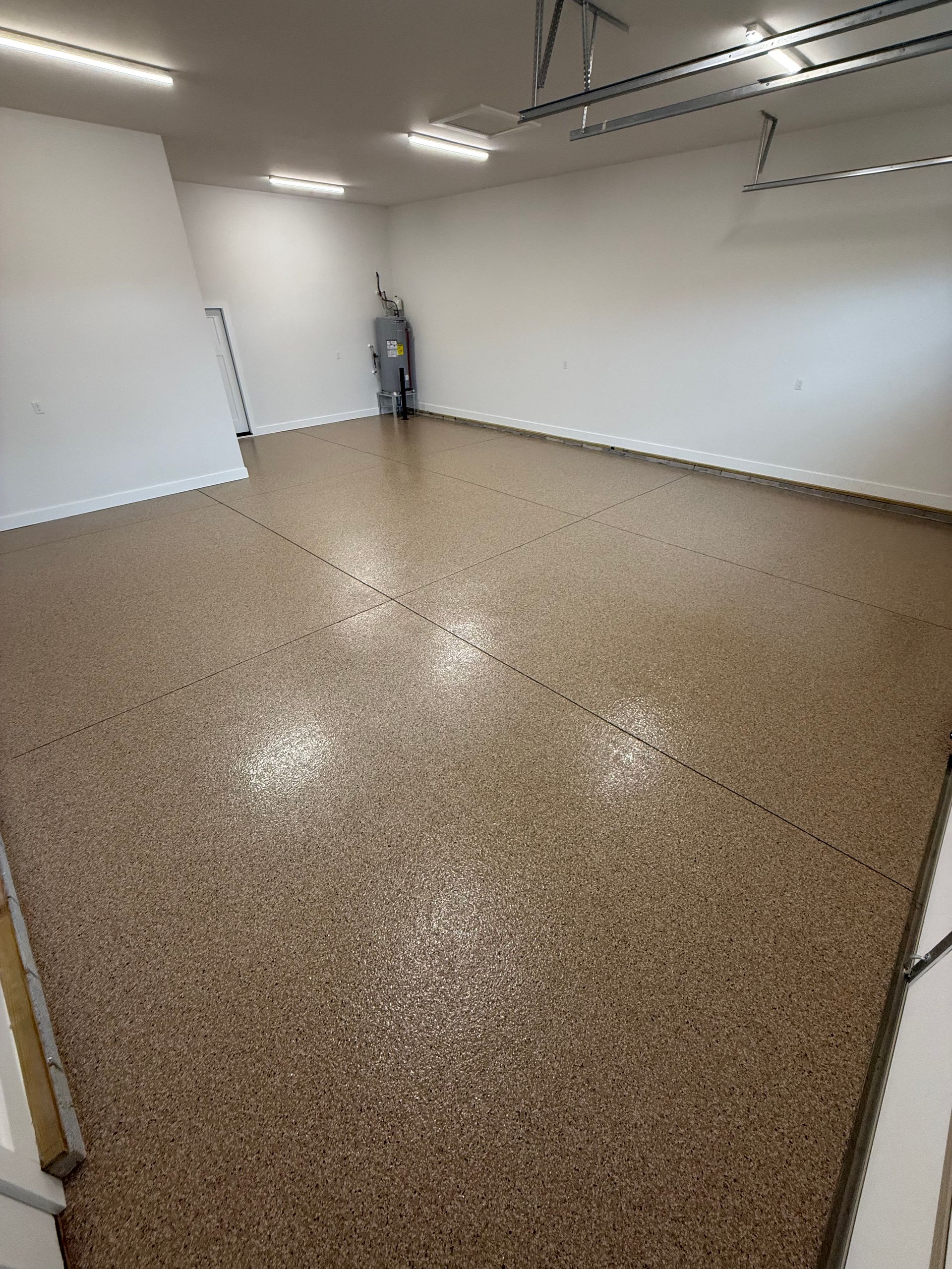 Empty garage with speckled epoxy floor, white walls, and overhead storage racks.
