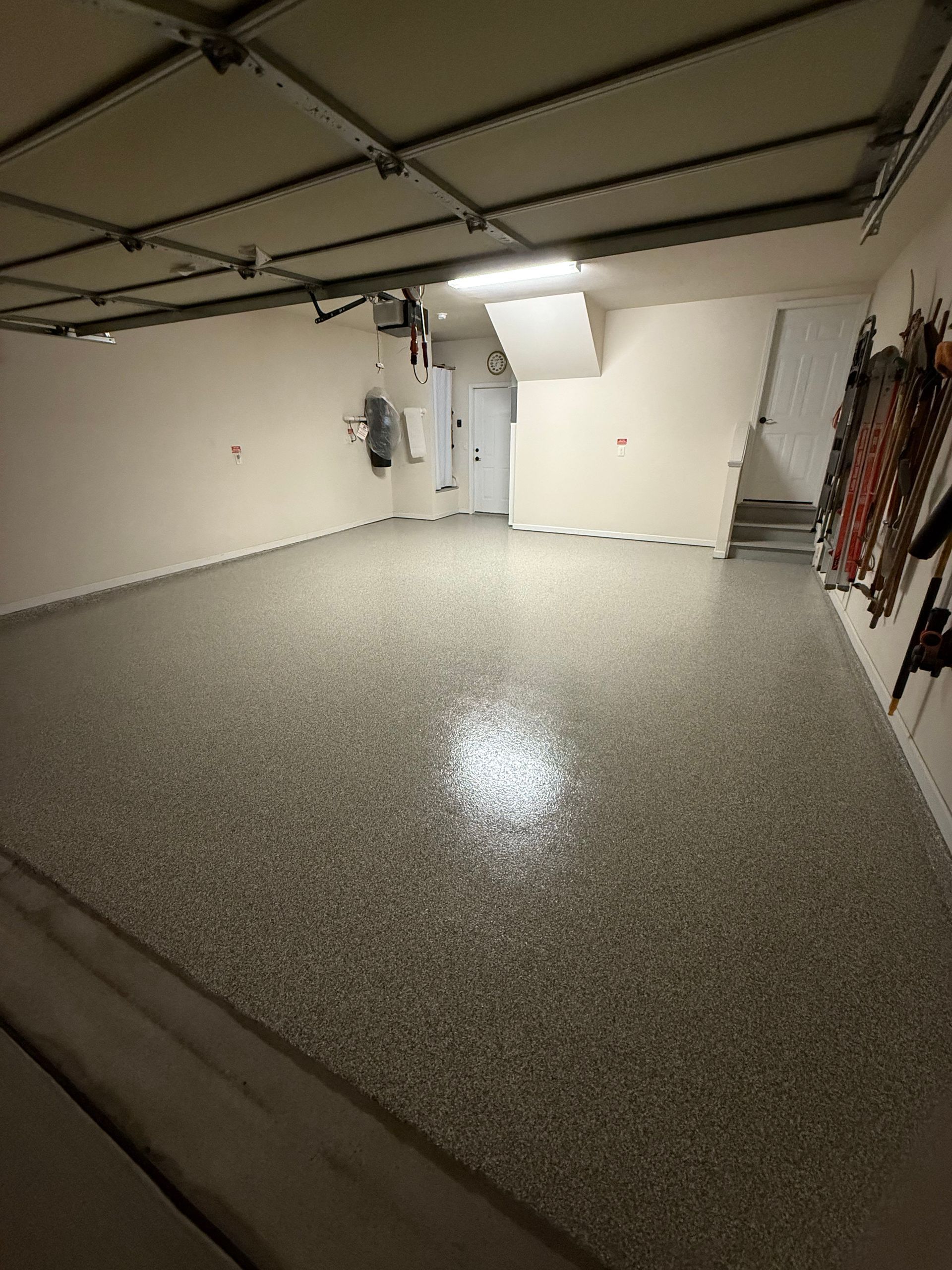 Empty garage with gray speckled floor, white walls, and closed door under fluorescent lighting
