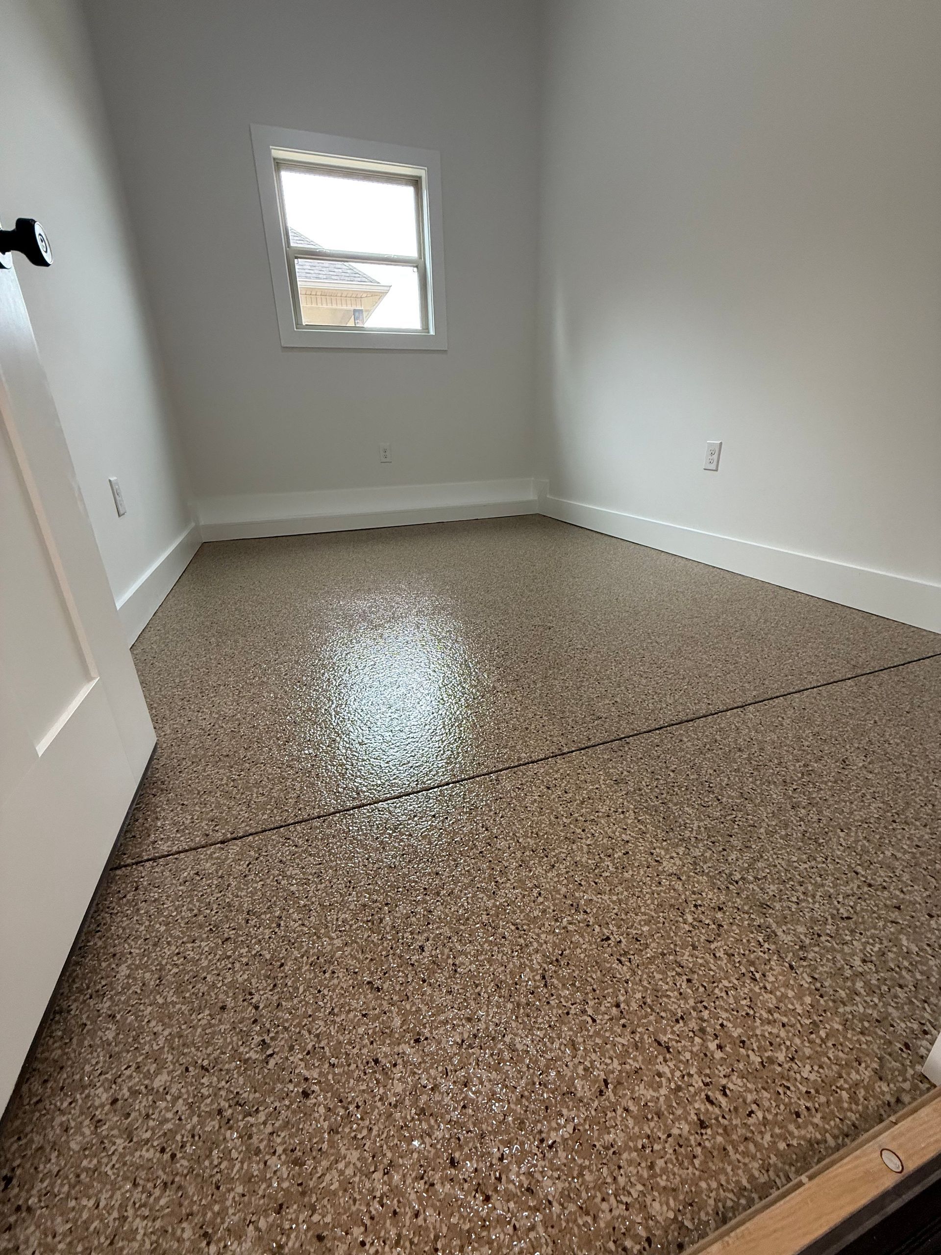 Empty white room with speckled brown floor and a small window.