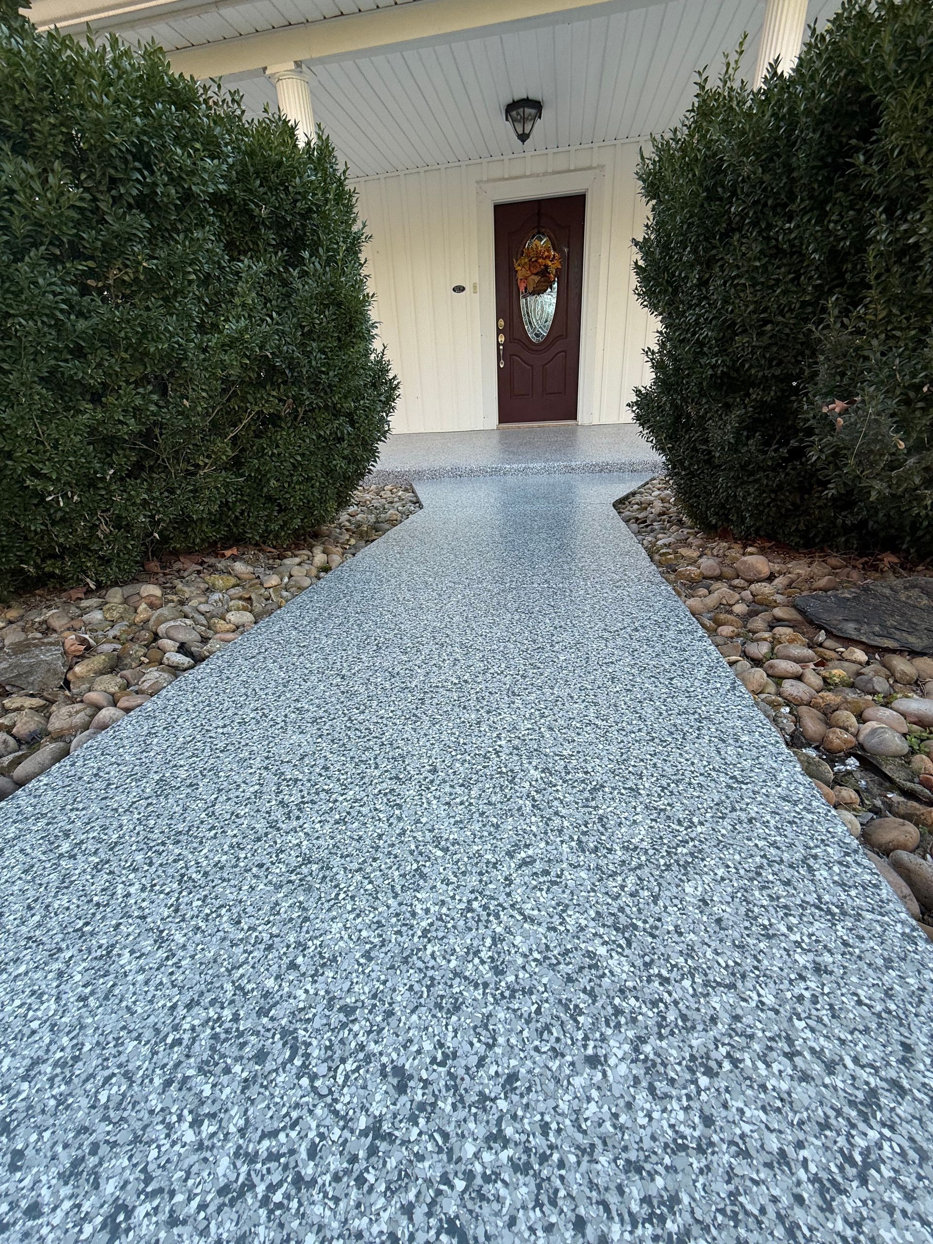 Front walkway of speckled blue stone leading to a white house door, flanked by trimmed bushes and rock borders