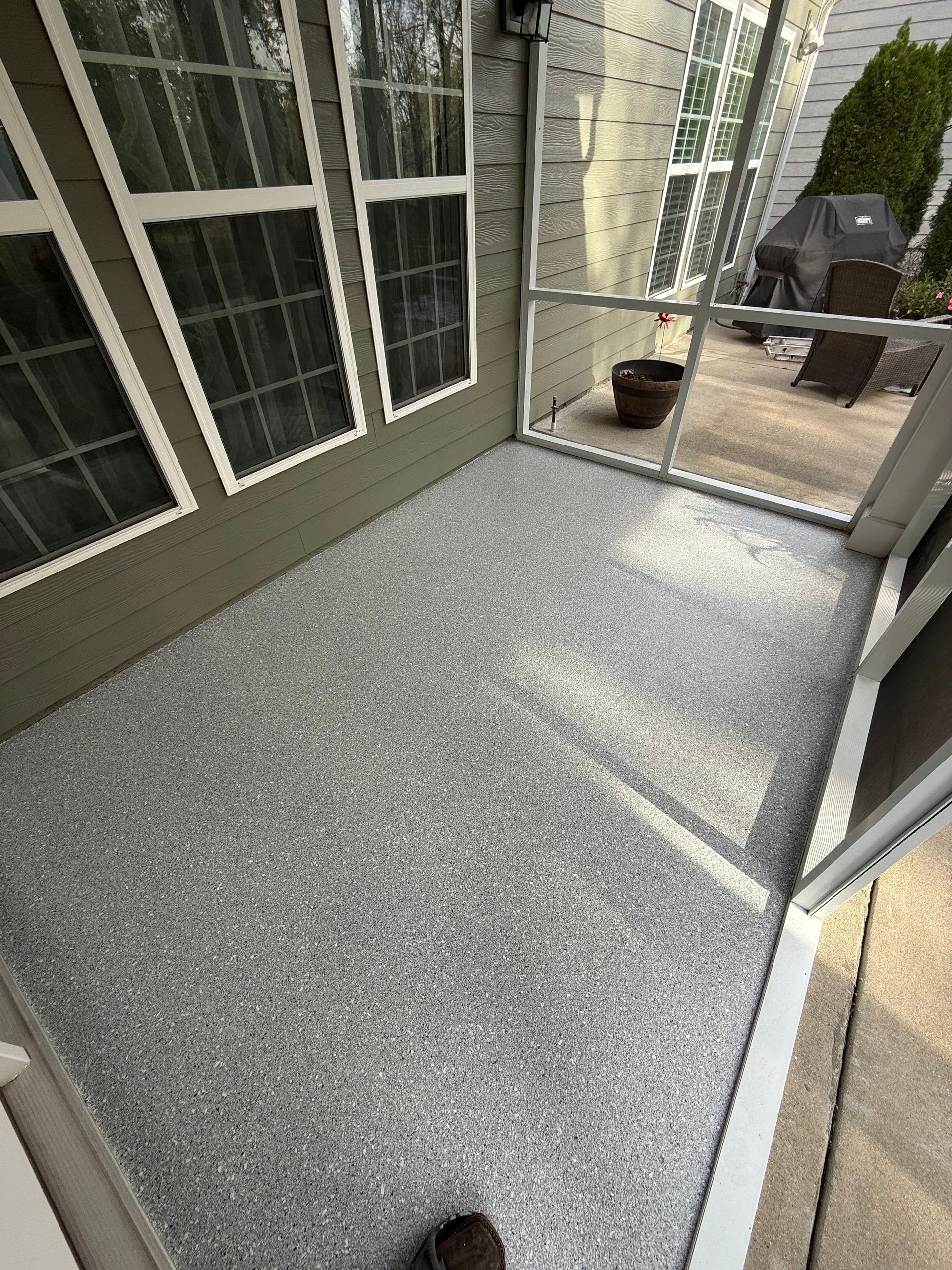 Small outdoor patio with gray speckled flooring, sliding glass doors, and a potted plant by a railing.