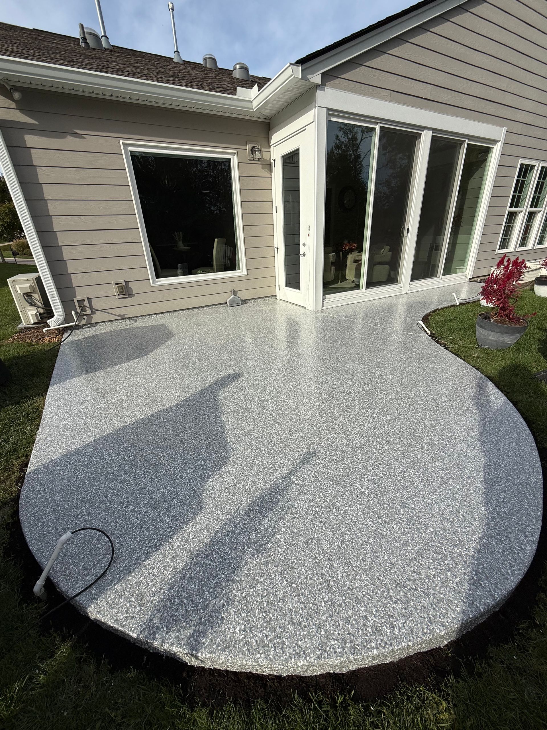 Round stone patio beside a house with large windows and a lawn edge