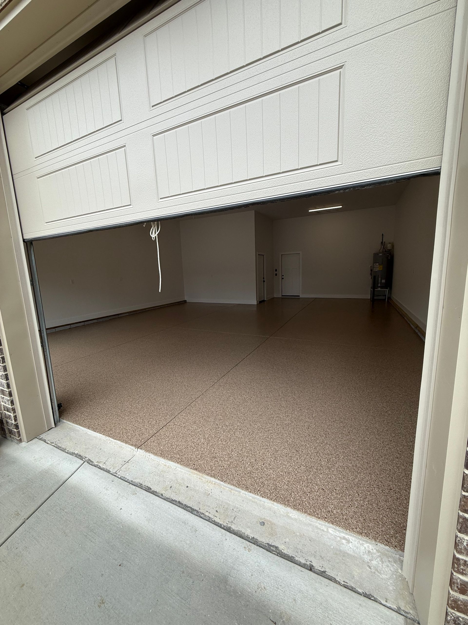 Partially open white garage door revealing an empty interior with brown floor and white walls