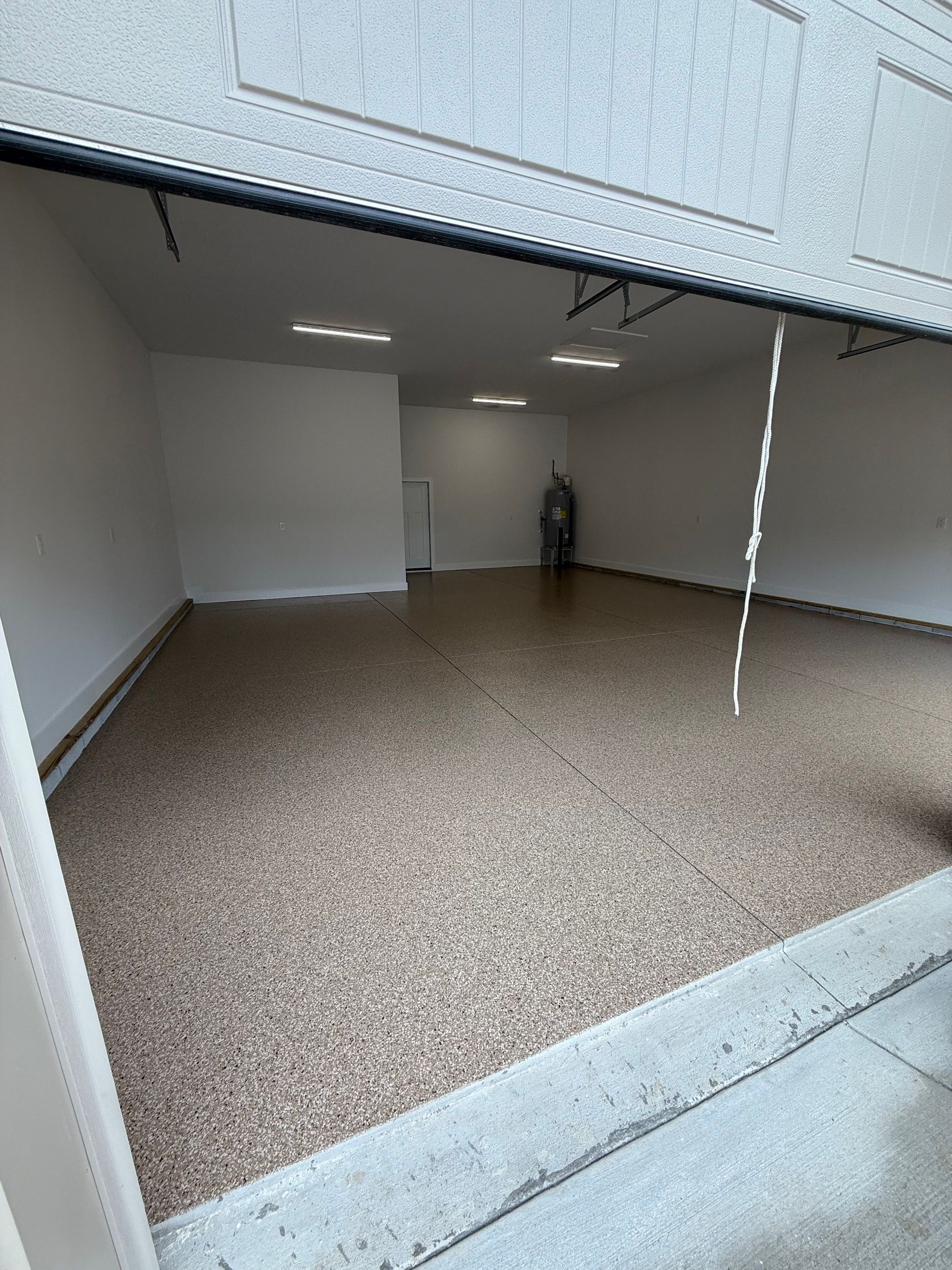 Empty indoor garage with white walls, speckled floor, and a small figure standing at the back.