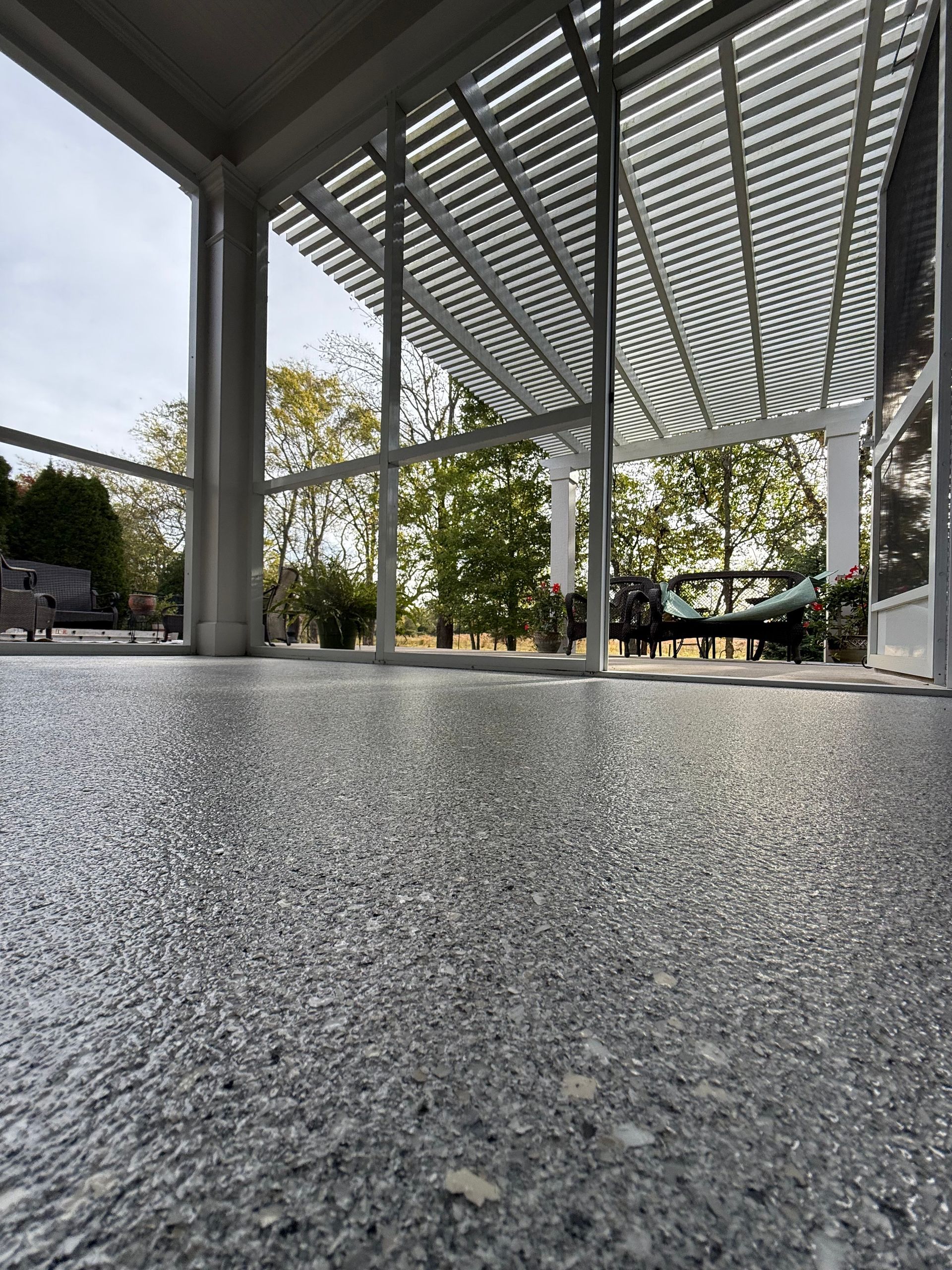 Low-angle view of a shaded outdoor pavilion with concrete columns and a textured floor under a slatted roof