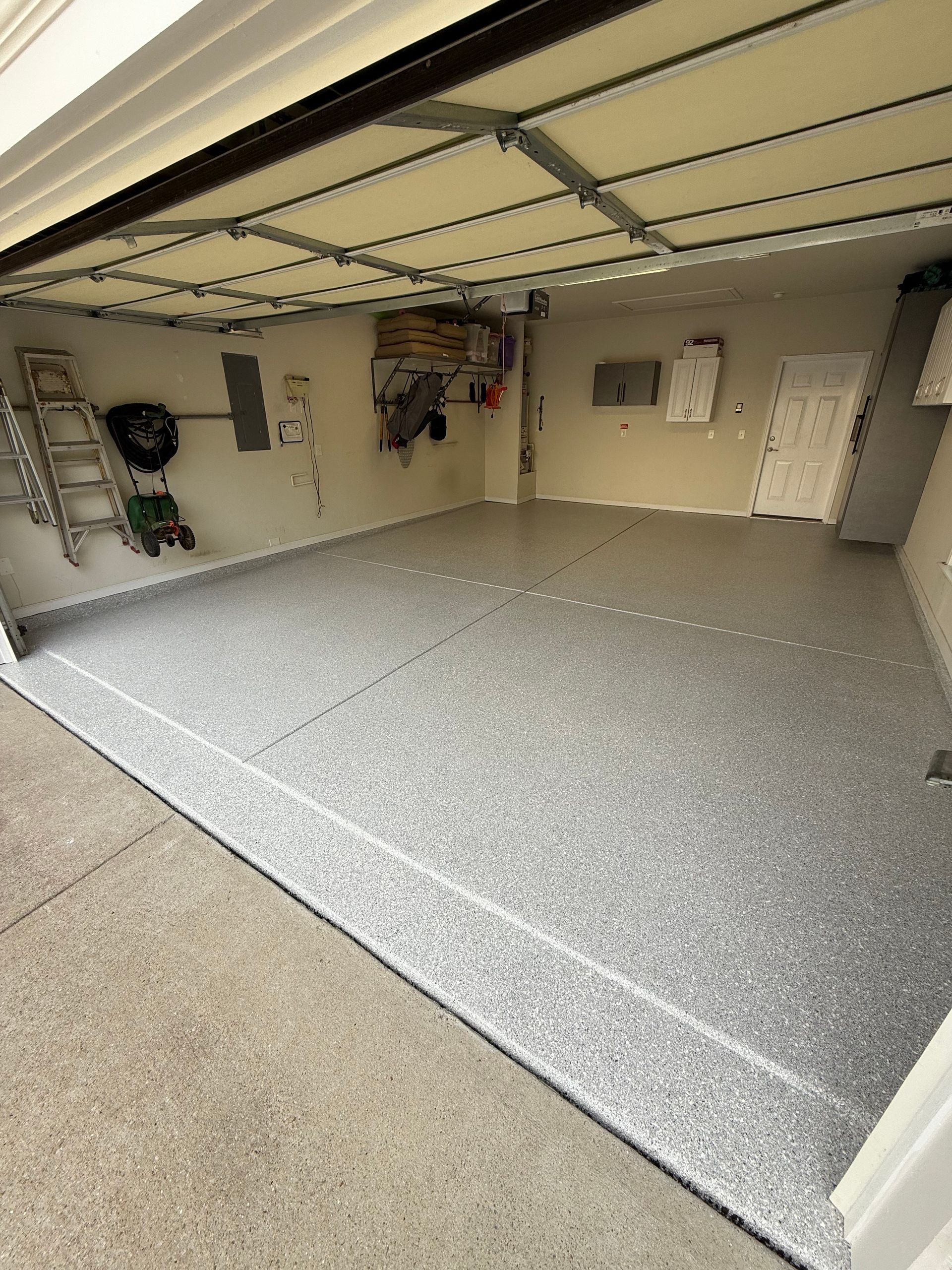 Empty garage with a speckled gray floor and open door, showing storage items on the walls.