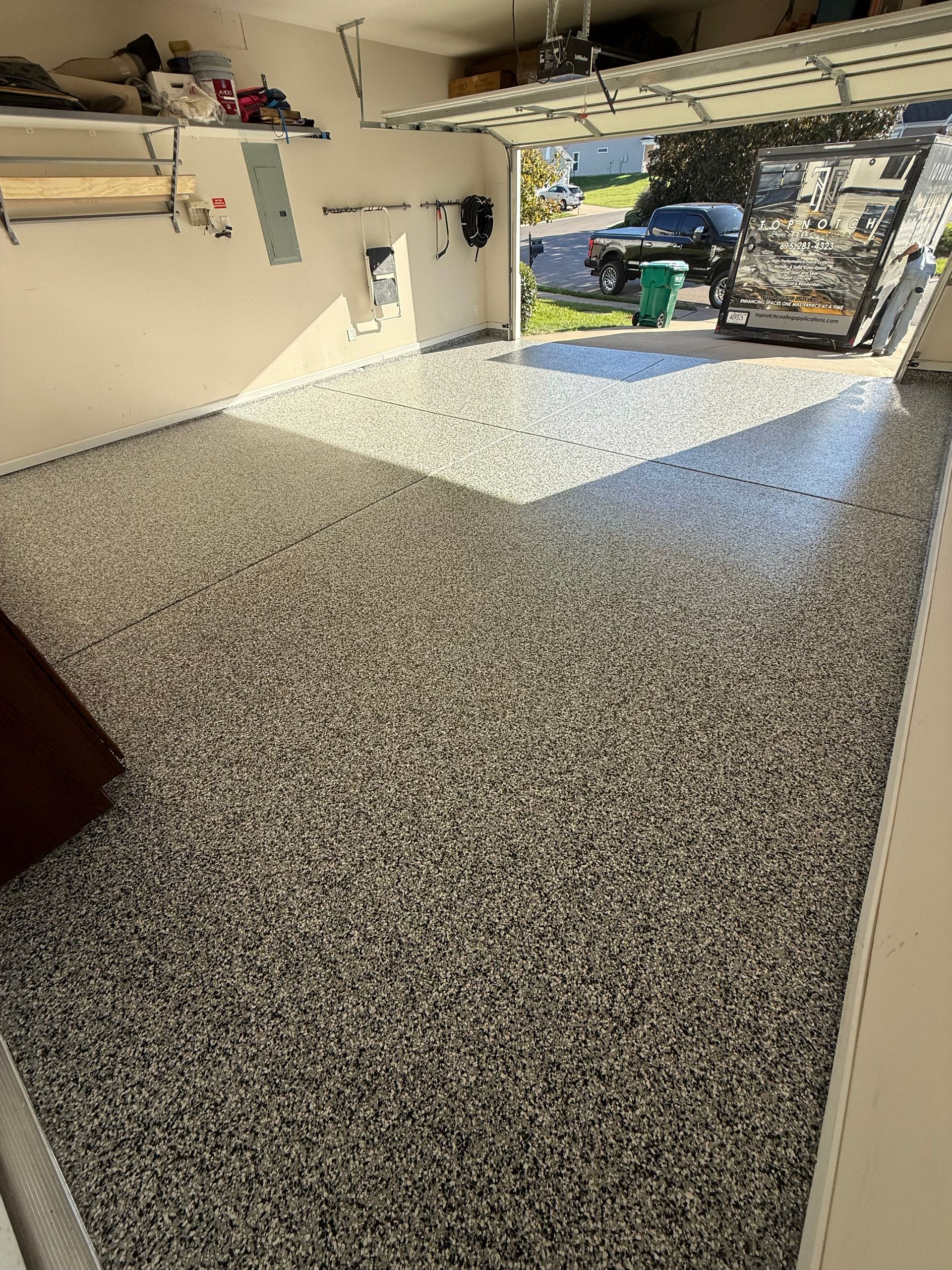 Speckled epoxy garage floor with open garage door and shelves along the wall