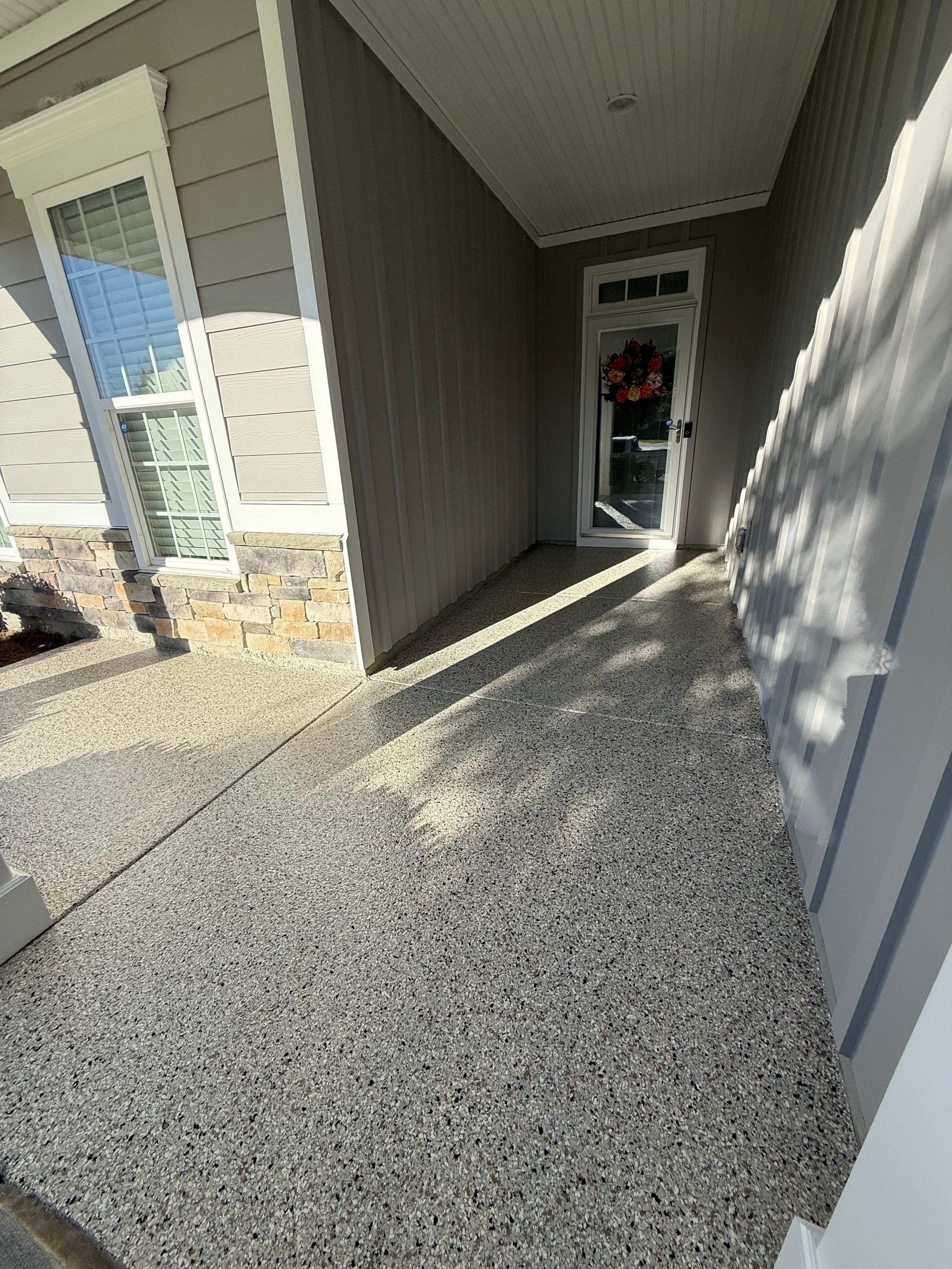 Gravel walkway between gray siding and white wall leading to an open doorway with a person inside