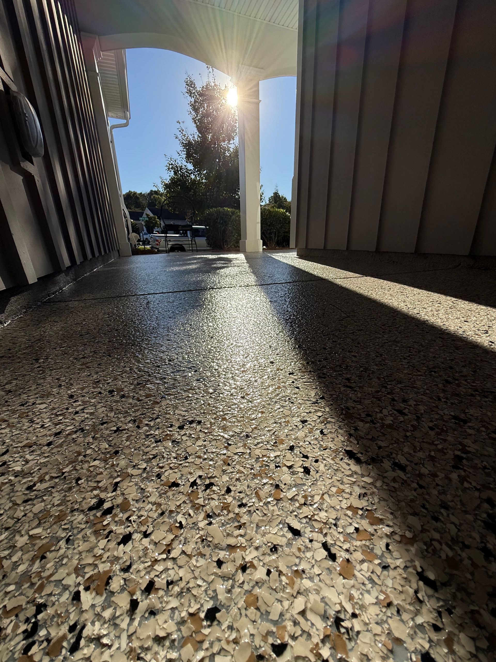 Sunlit driveway between two buildings, with a bright beam of light and long shadows on textured pavement.