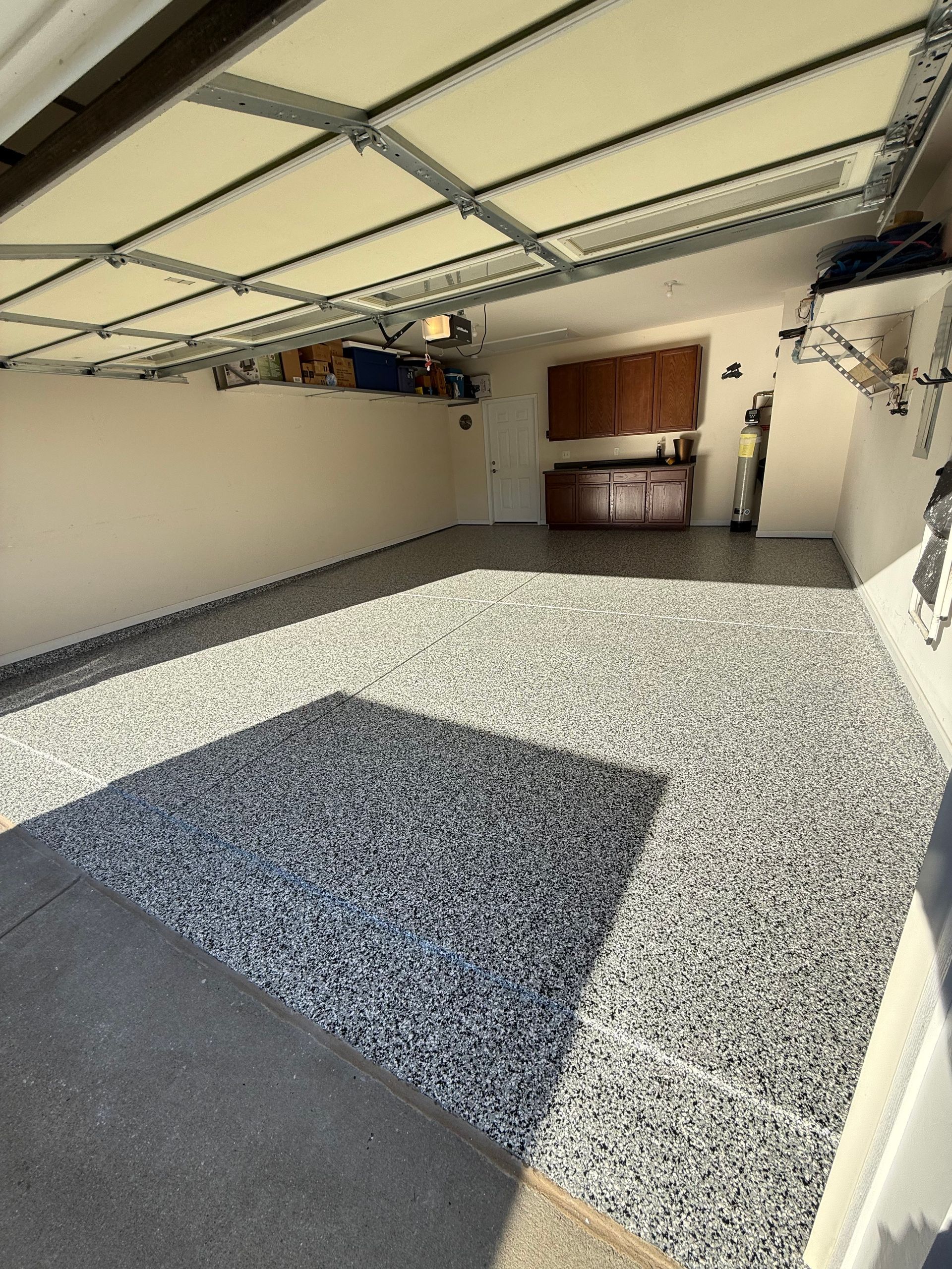 Empty garage with open door, gray speckled floor, and shelves along the back wall
