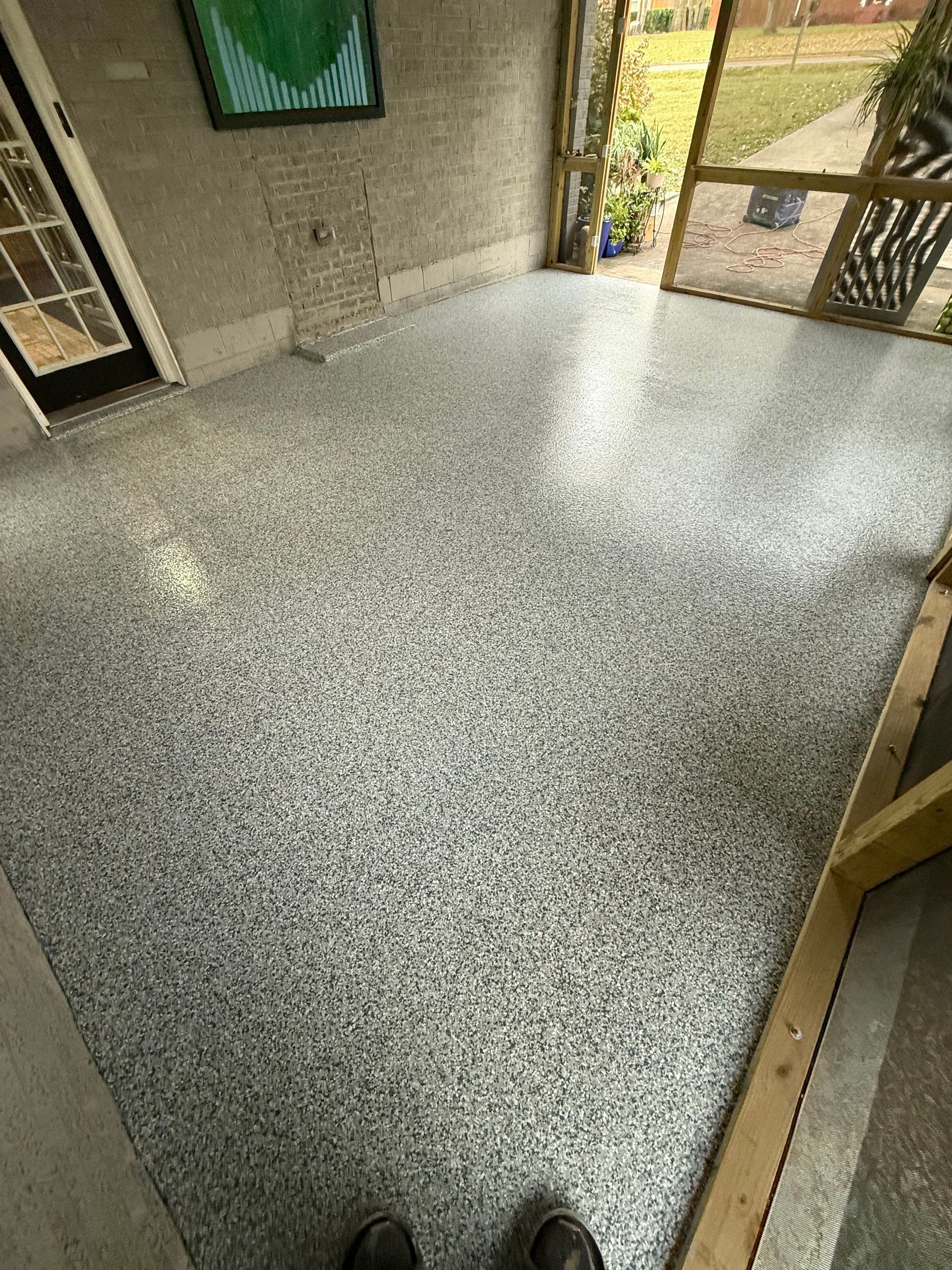 Speckled terrazzo floor in an entrance area, with doors and a person’s shoes visible at the bottom.