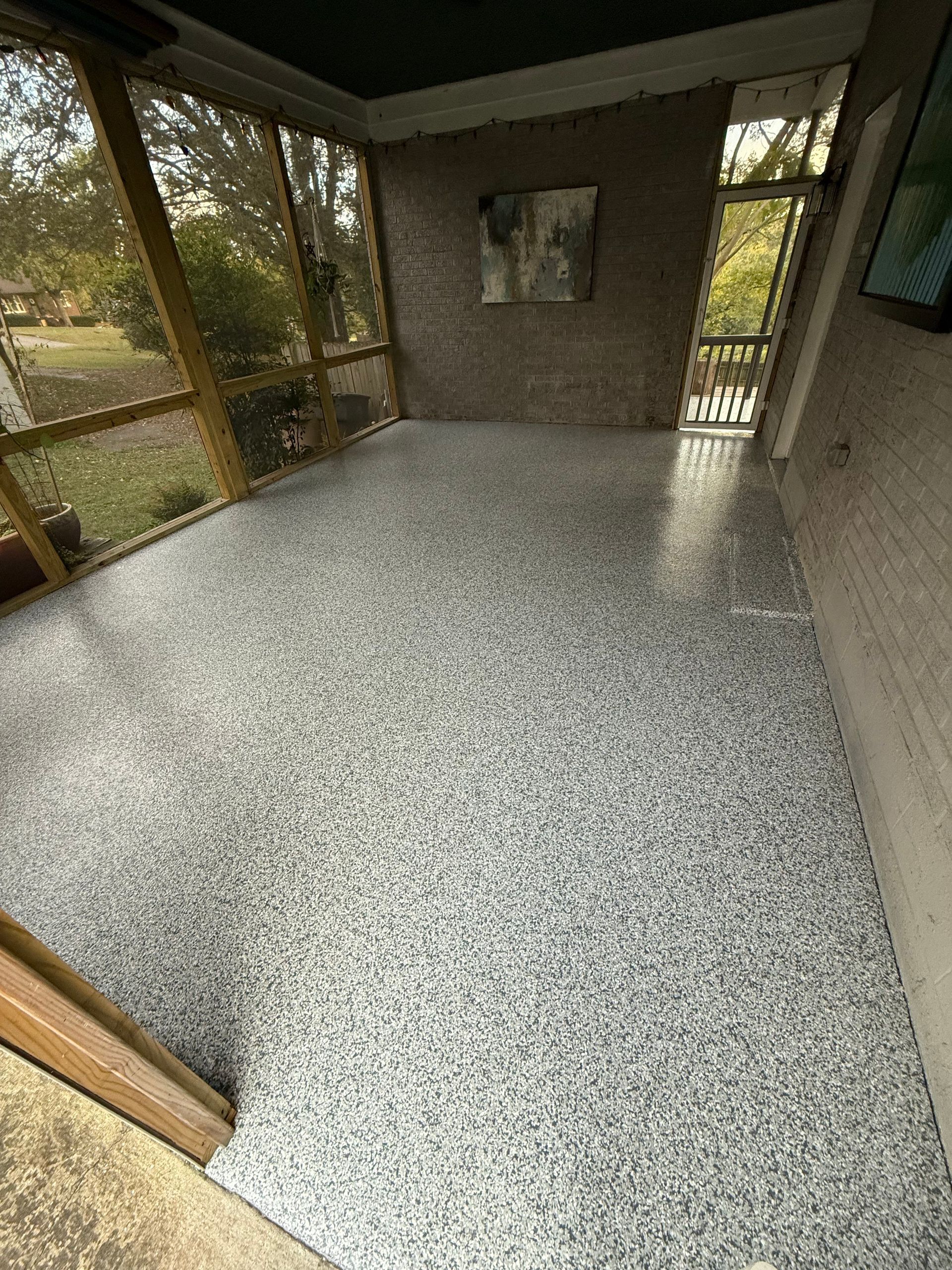 Empty screened porch with speckled concrete floor and windows overlooking trees