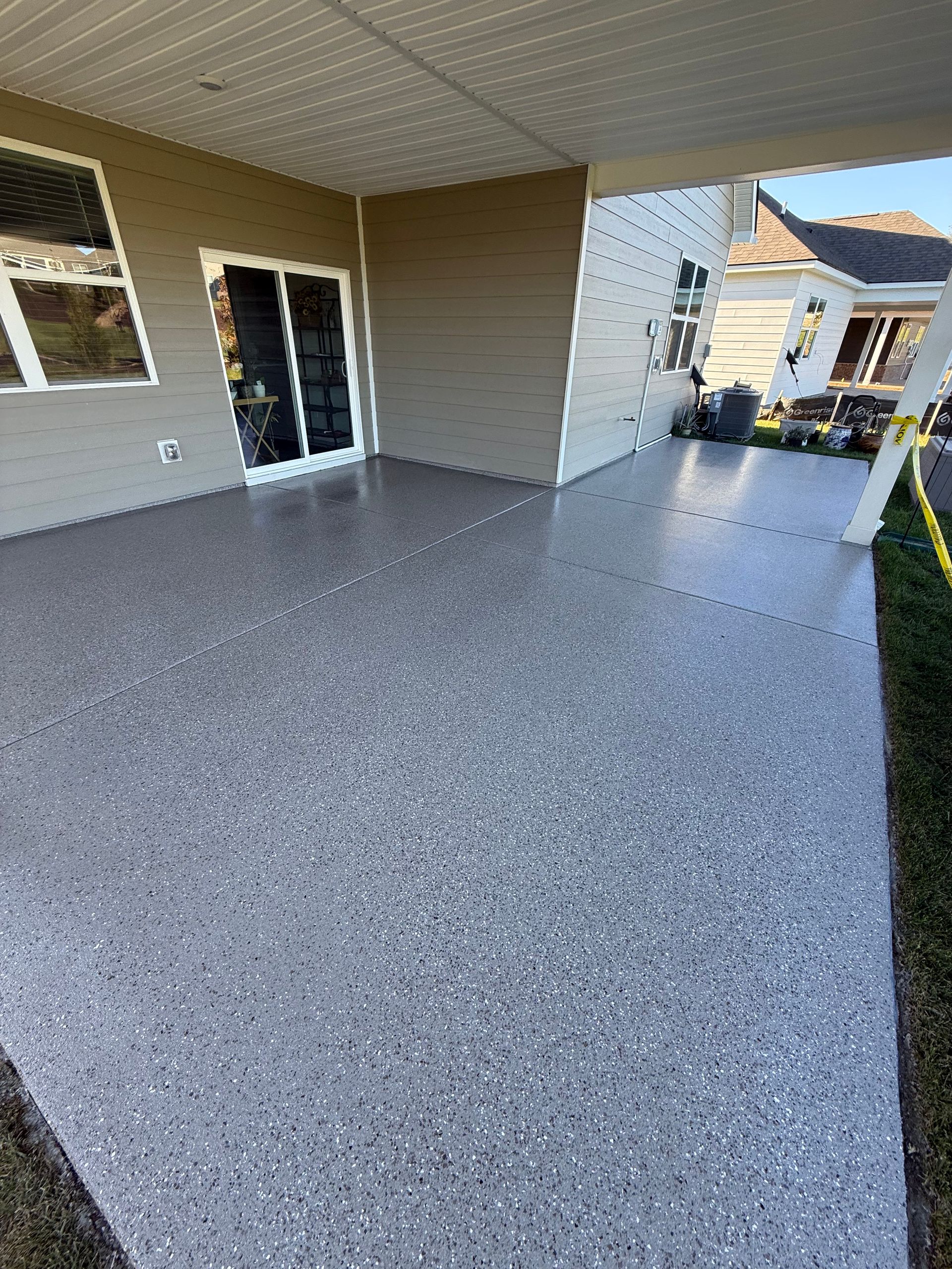 Covered front patio with speckled concrete floor and sliding glass doors opening to a yard.