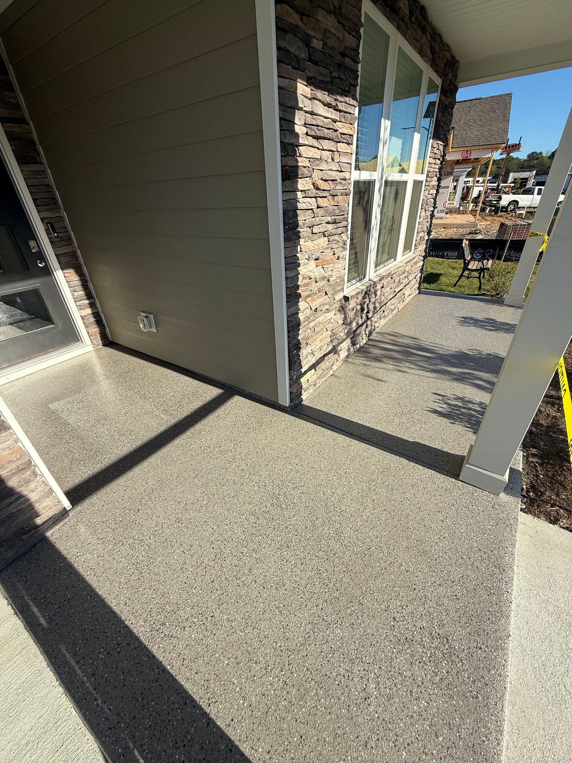 Covered outdoor walkway with stone and siding, looking out toward a grassy area and houses.