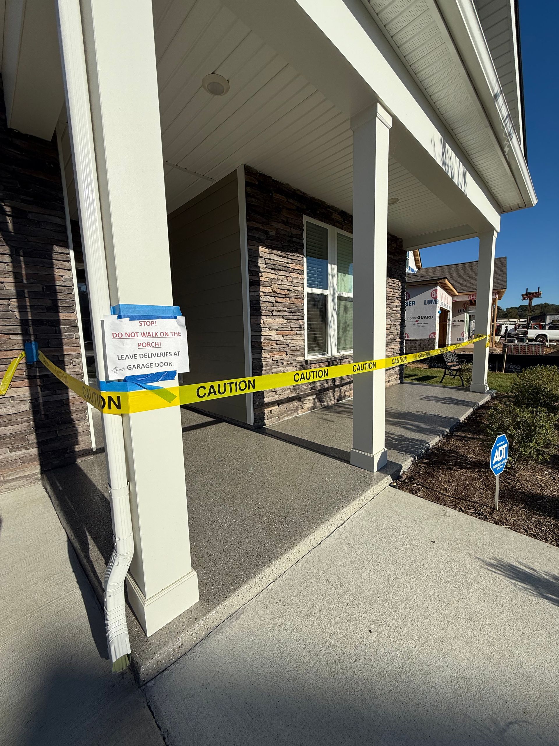 Caution tape blocks the entrance of a building with stone columns and white siding.
