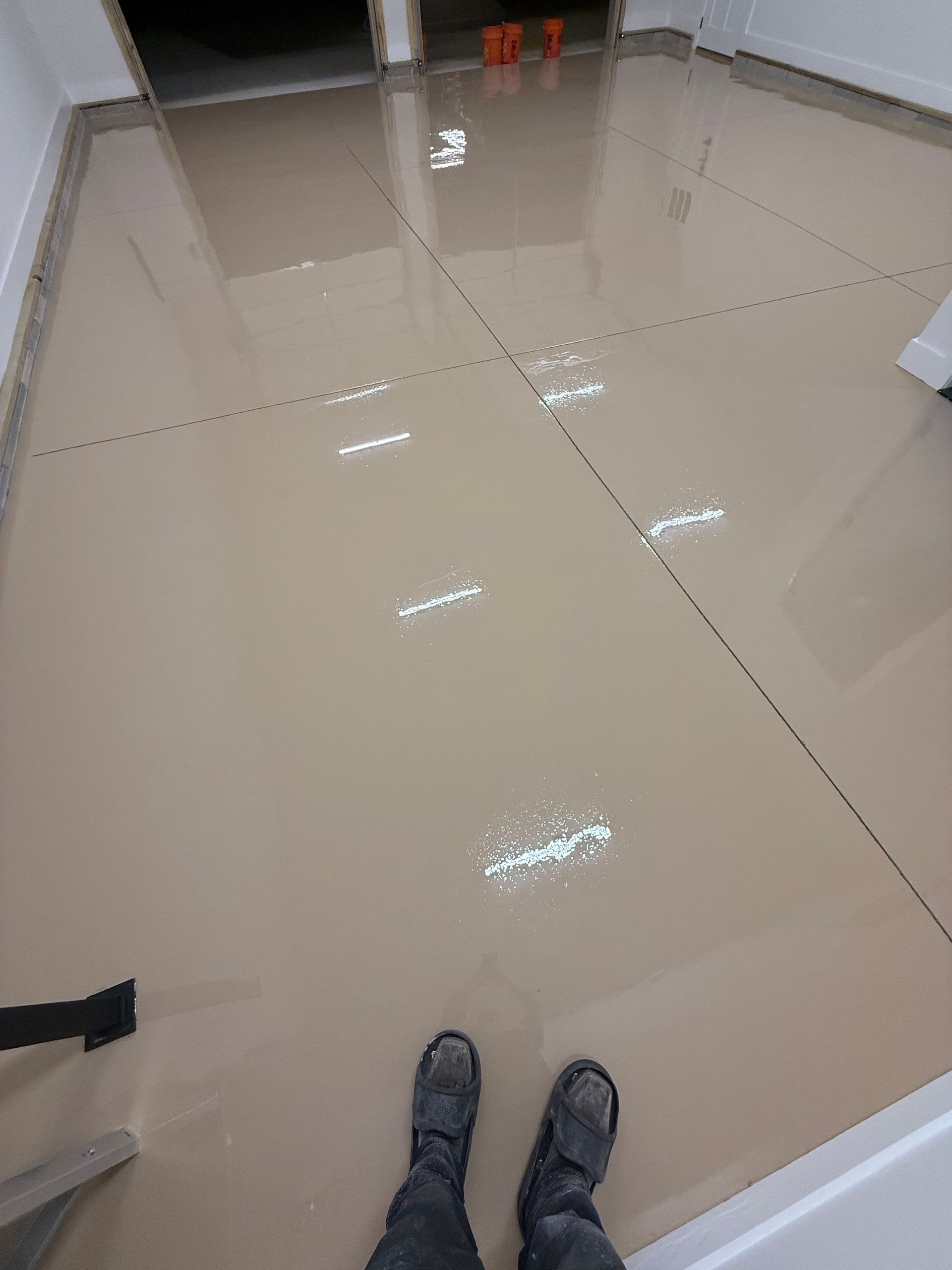 Shiny tiled floor in a room, with a person’s shoes visible at the bottom edge.