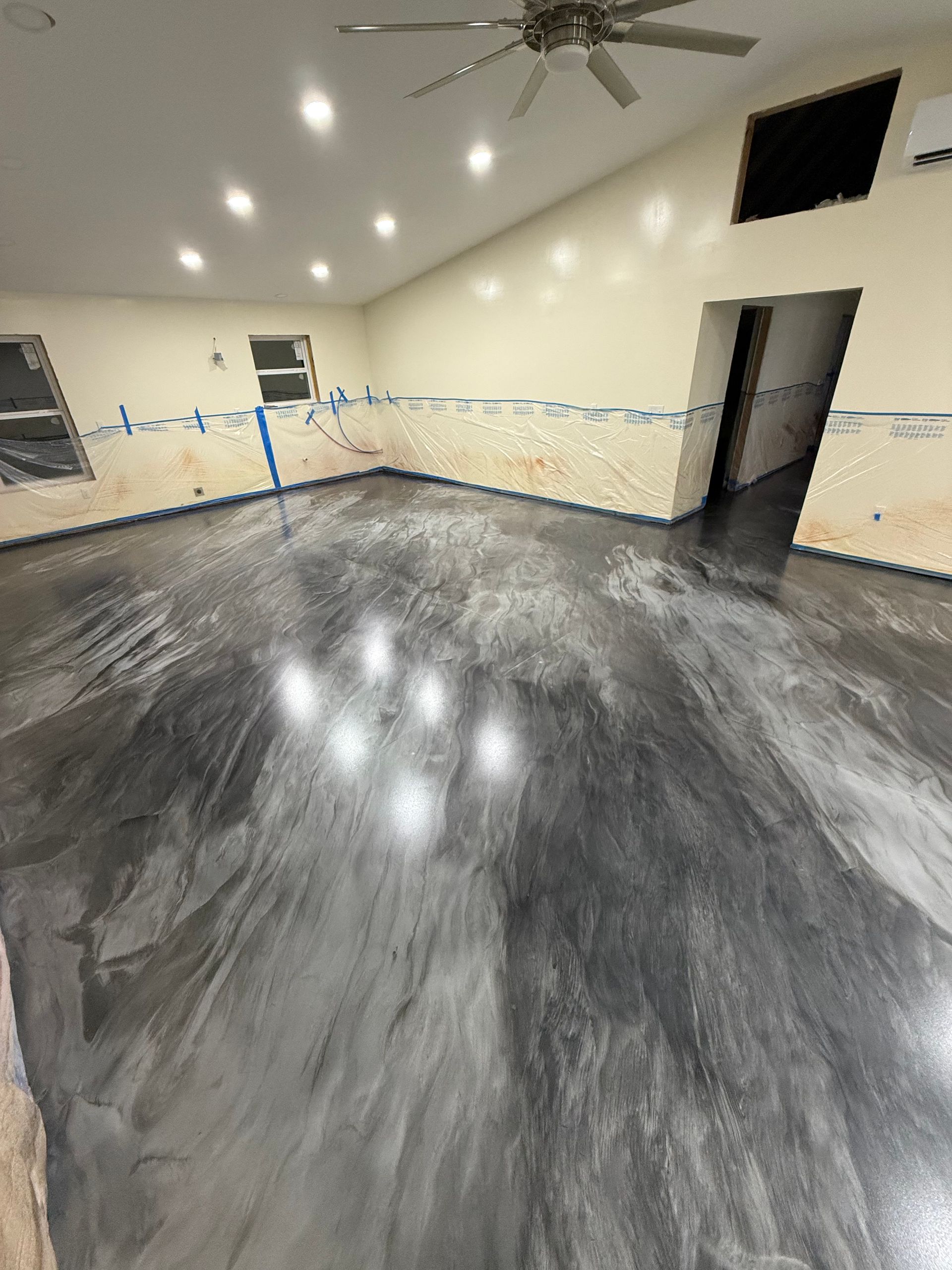 Empty room with gray wood floor, beige walls, ceiling fan, and recessed lights reflecting on the floor