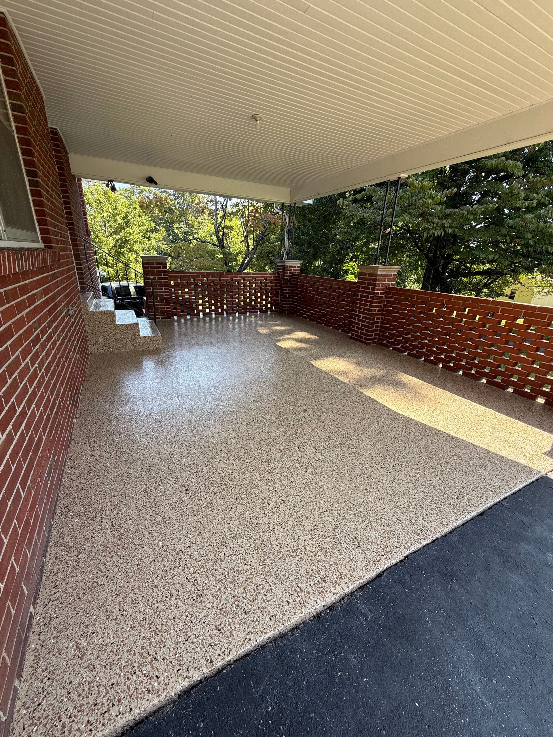 Covered porch with speckled floor, brick railing, and trees outside
