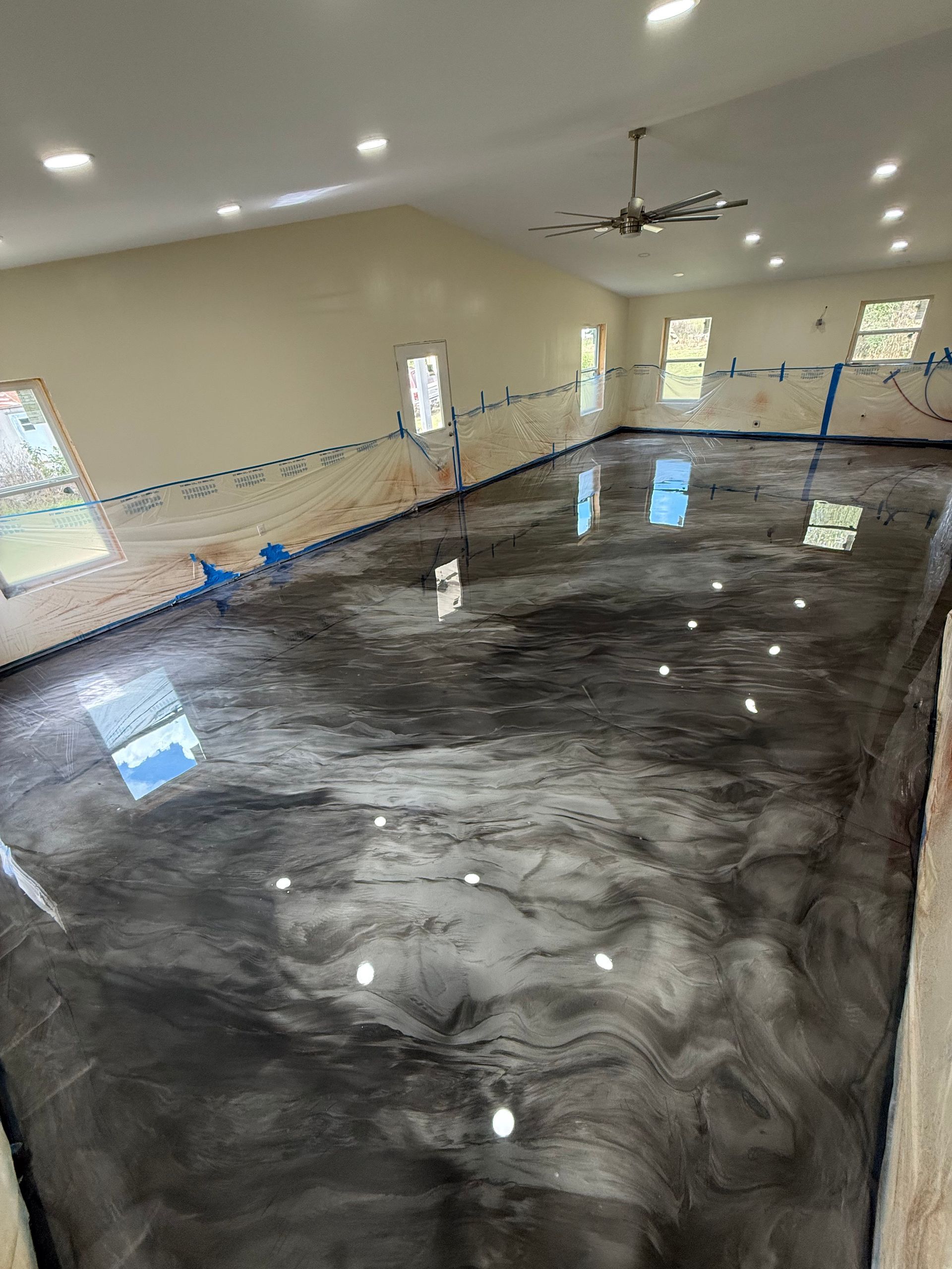 Shiny black epoxy floor in a large empty room with recessed lights and windows along the walls