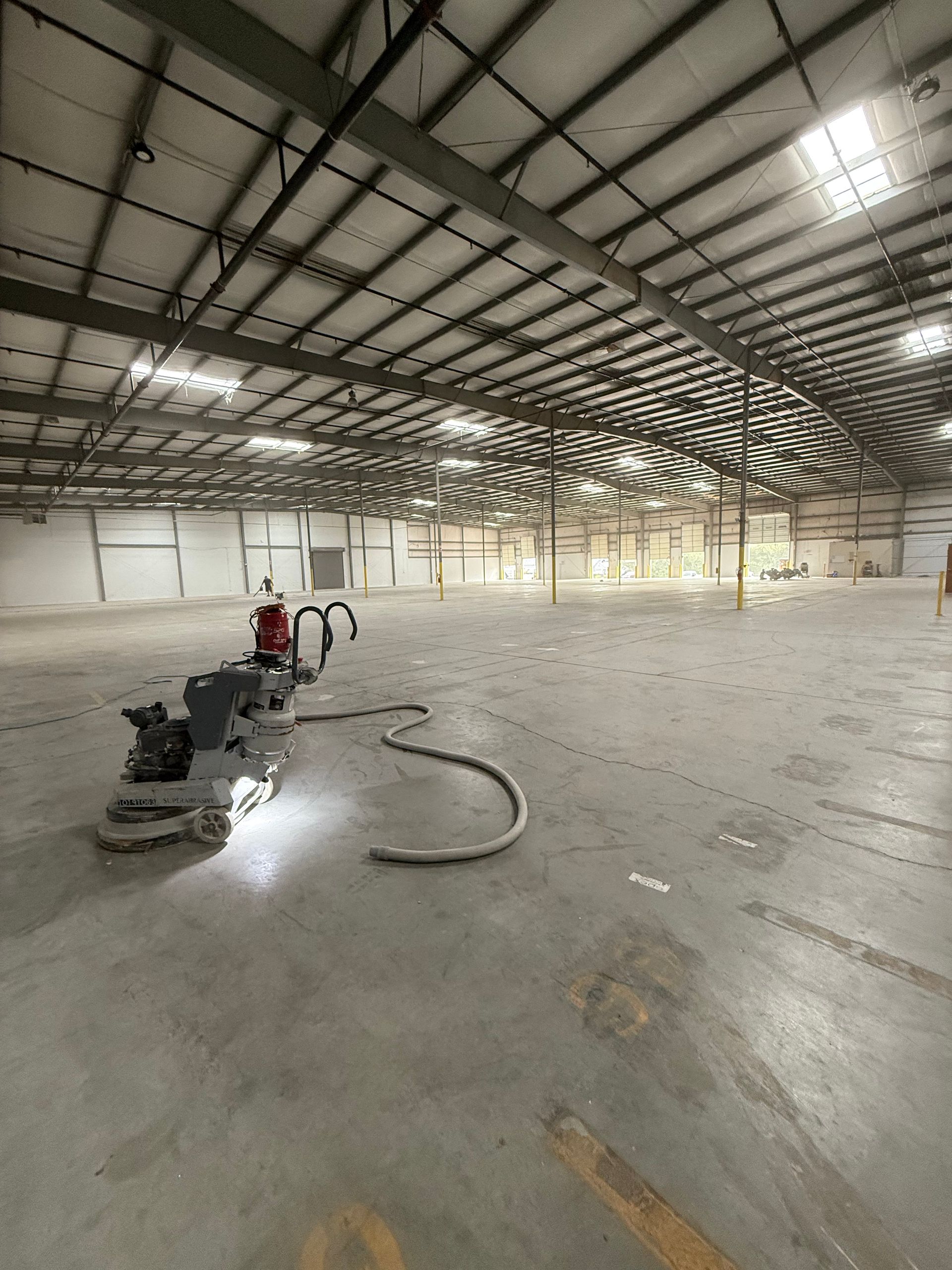 Empty warehouse with a floor grinder and hose on a concrete floor under bright overhead lights