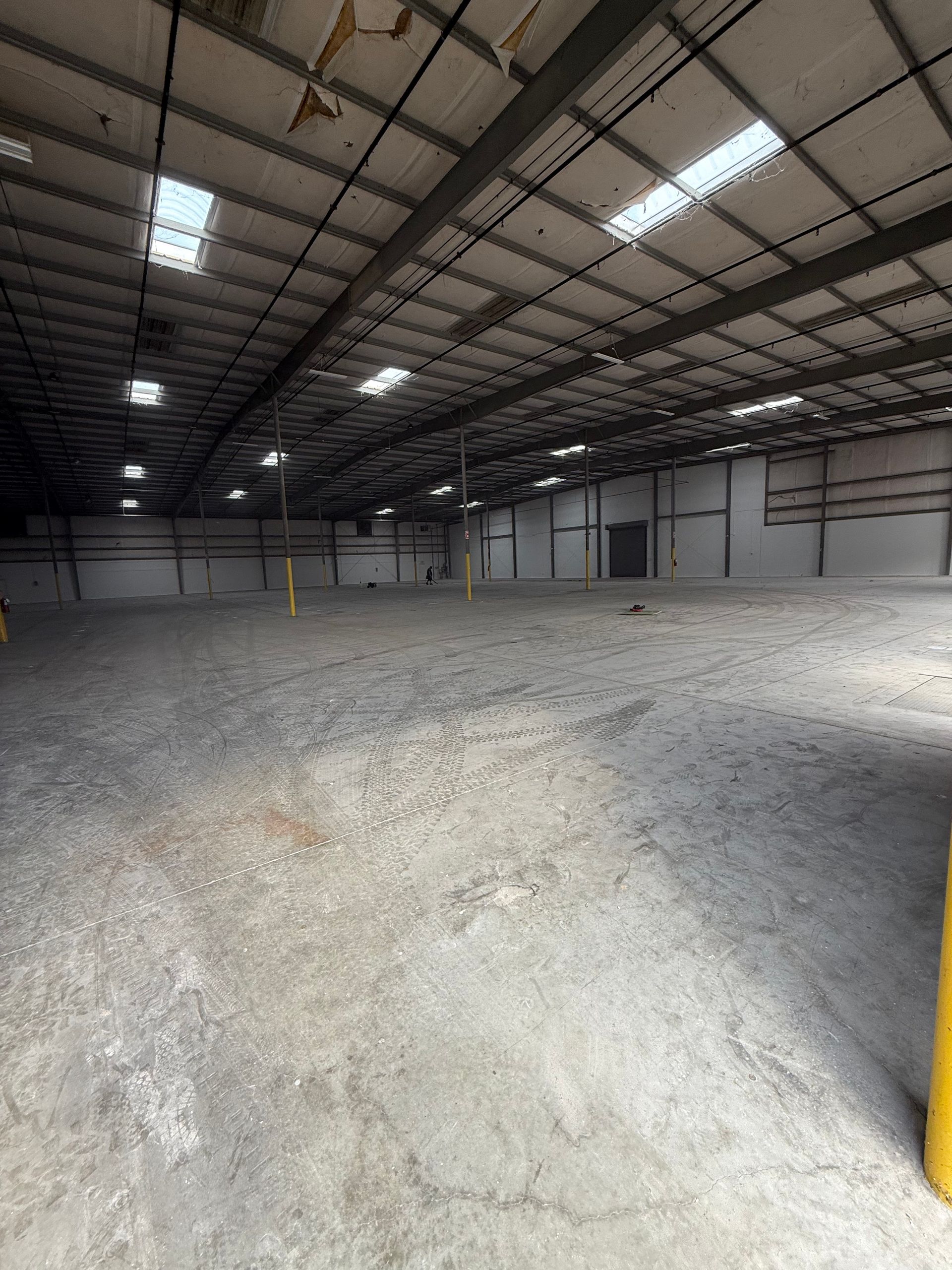 Empty warehouse interior with gravel floor, metal roof, and skylights illuminating the space