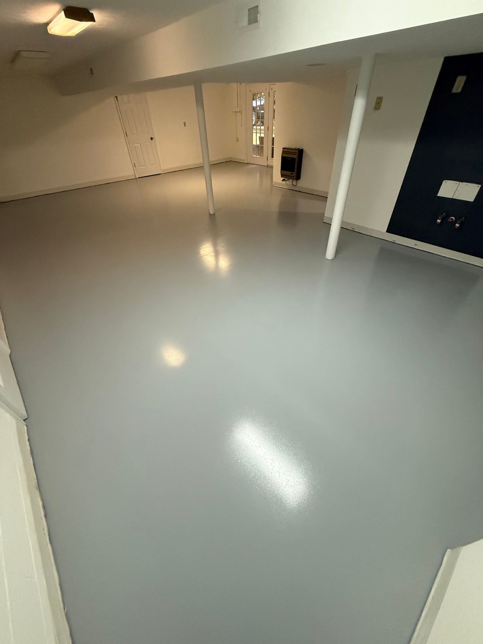 Empty bright room with glossy gray floor, white walls, and a dark door on the right