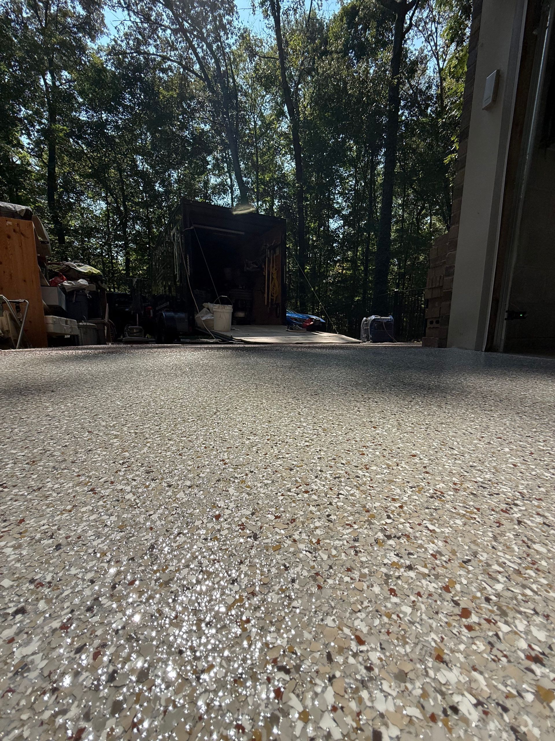 Low-angle view of a gravel driveway beside a wooded yard and buildings in bright sunlight