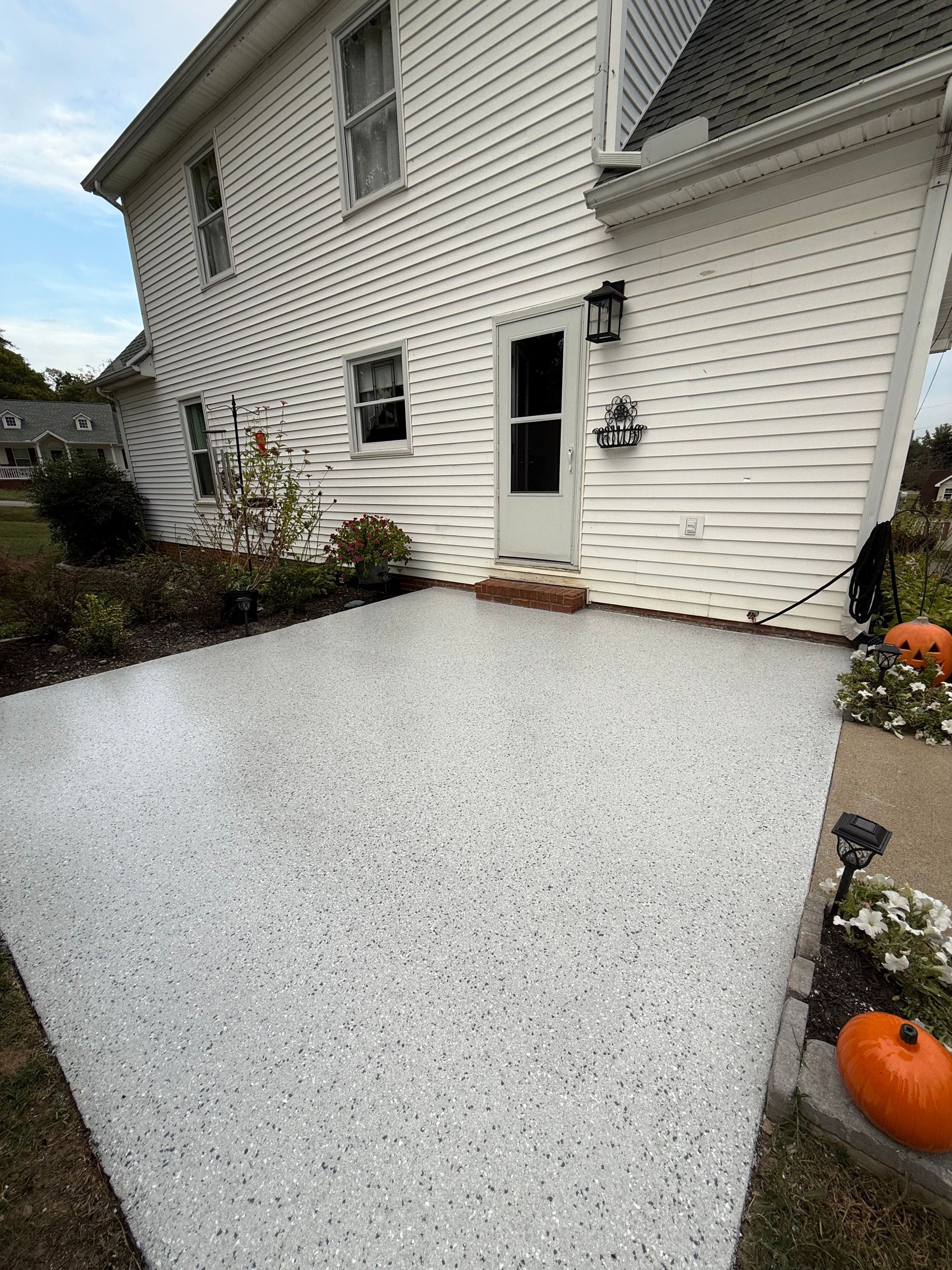 White pebble-coated front patio with a house entrance, black door, and pumpkins by the steps.