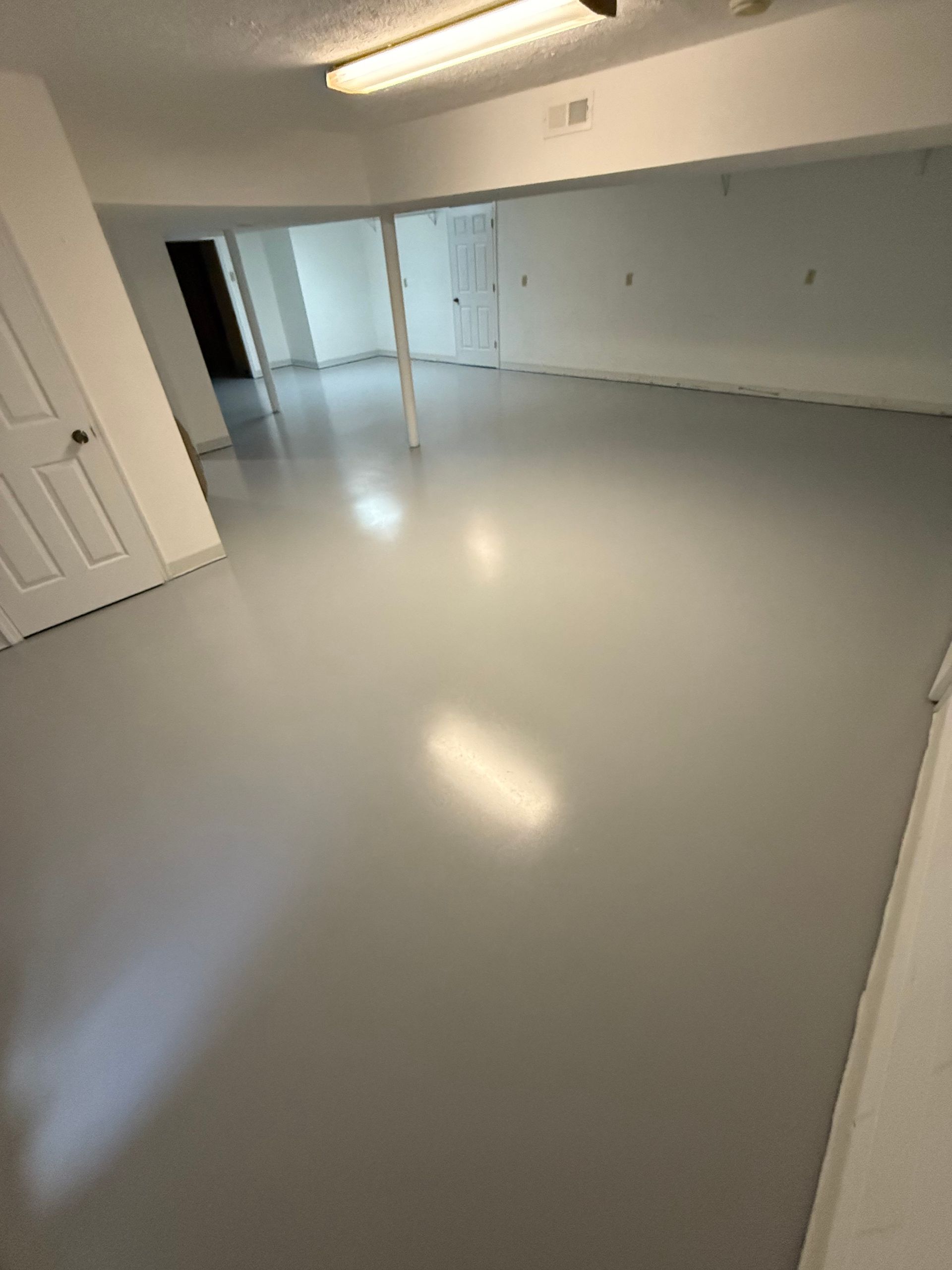 Empty white room with glossy floor, fluorescent ceiling lights, and open doorway to a hallway