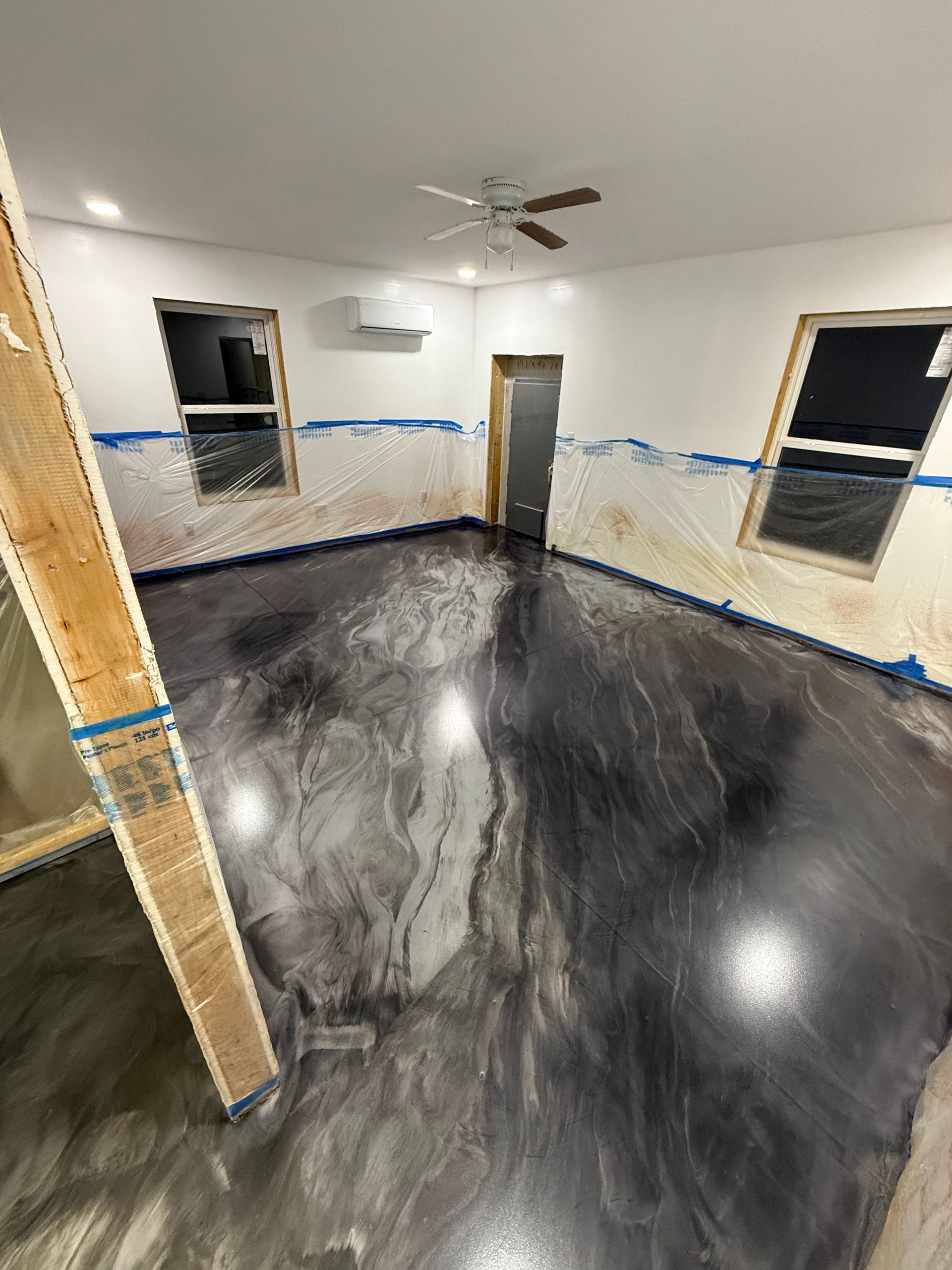 Empty room with dark polished floor, white walls, windows, and a ceiling fan.