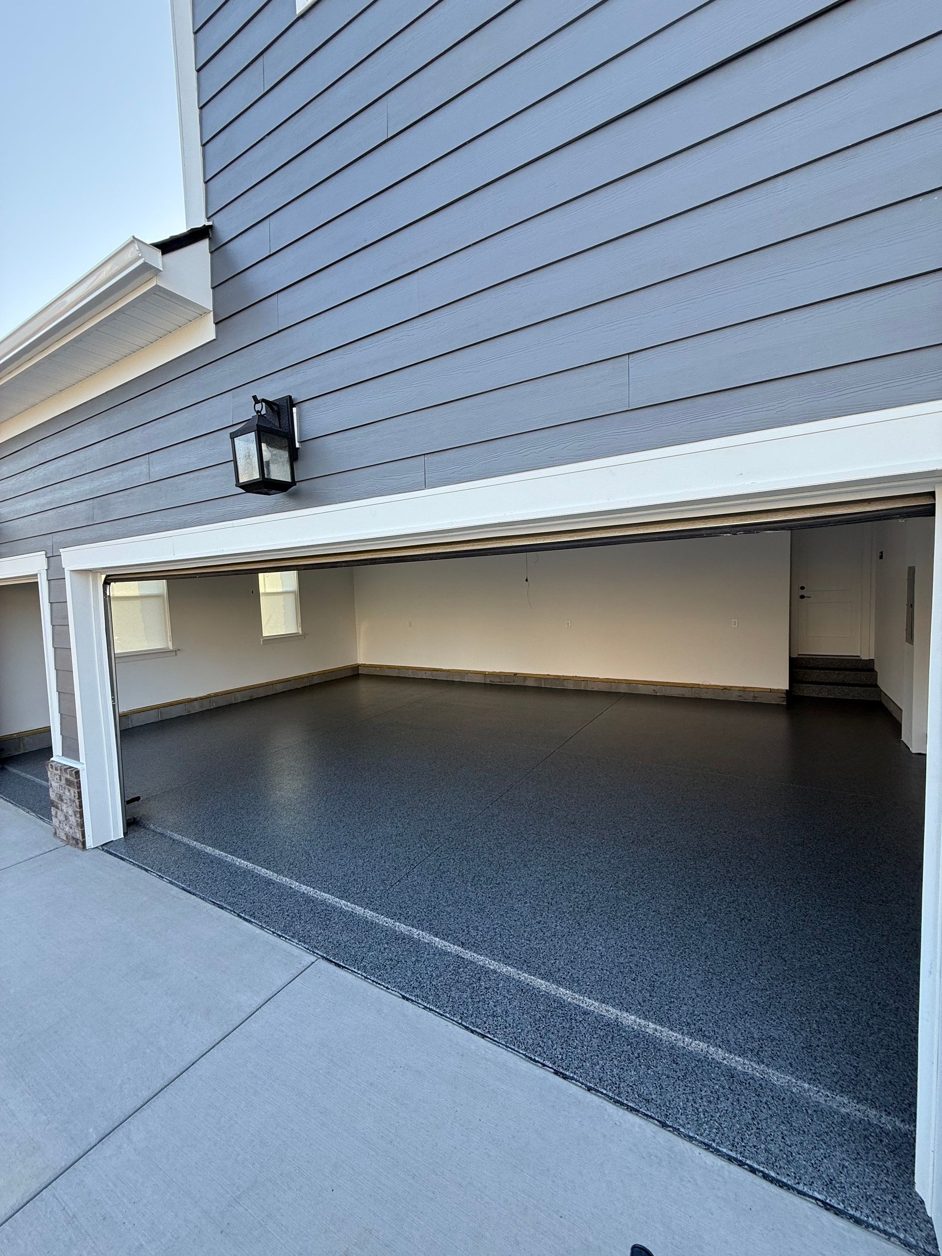 Open garage with gray siding and speckled epoxy floor, viewed from the driveway.