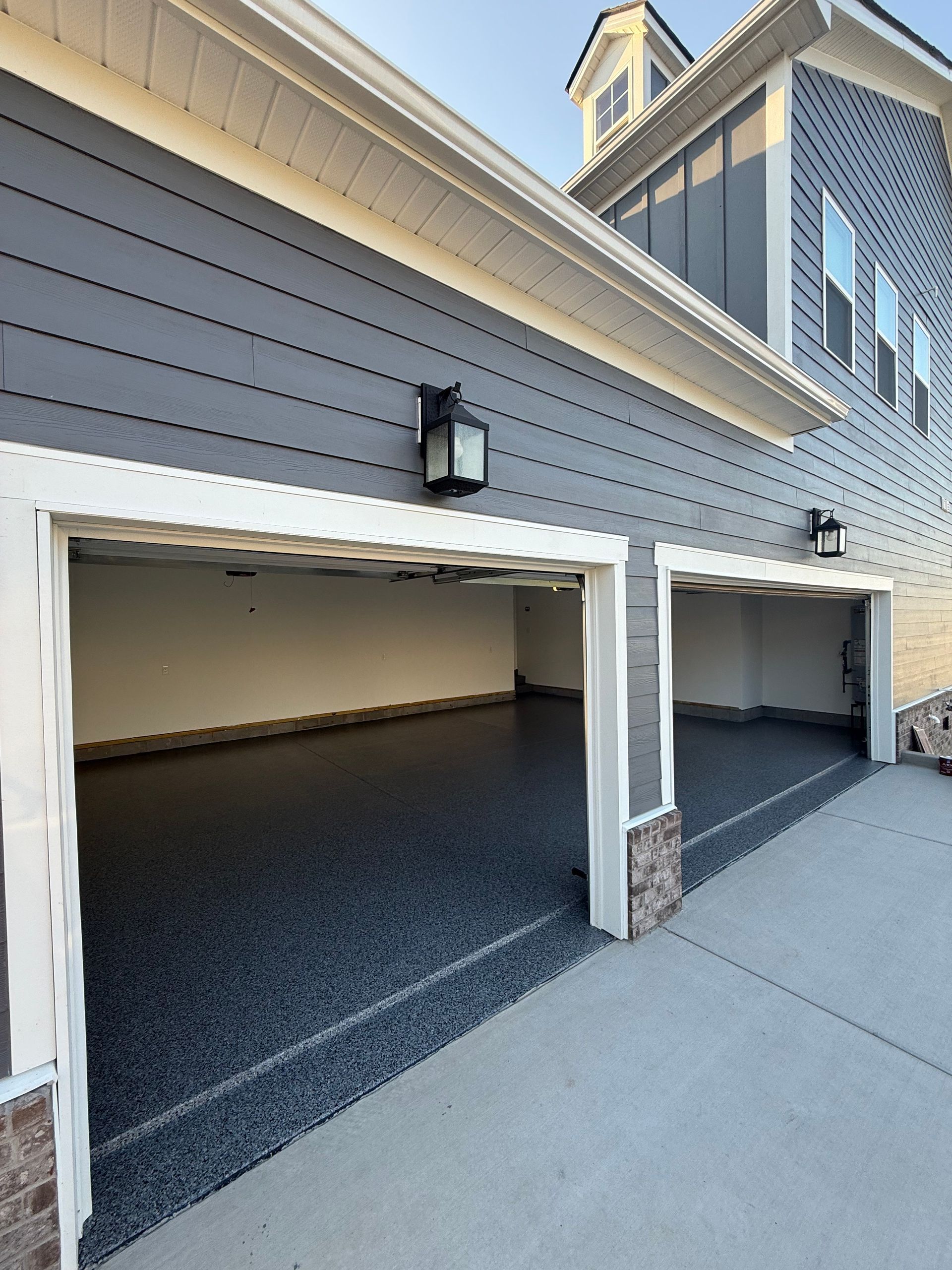 Two empty garages with open white doors beside a gray-sided building and sidewalk